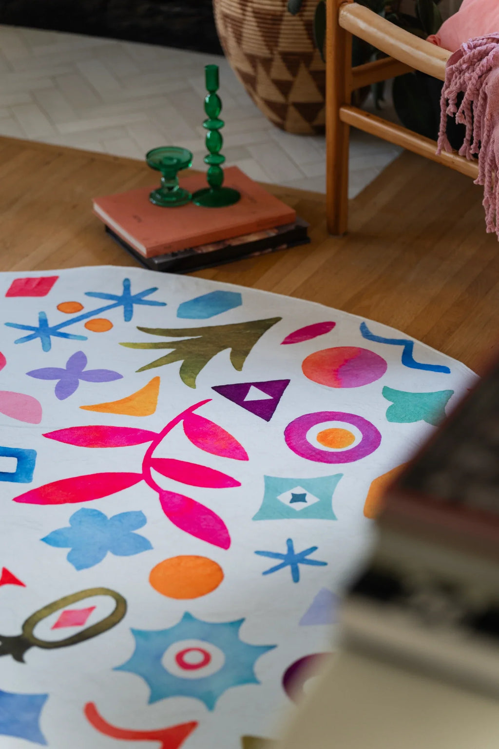 Partial round area rug beside a green lamp and books, showing multicolor symbols on a white background