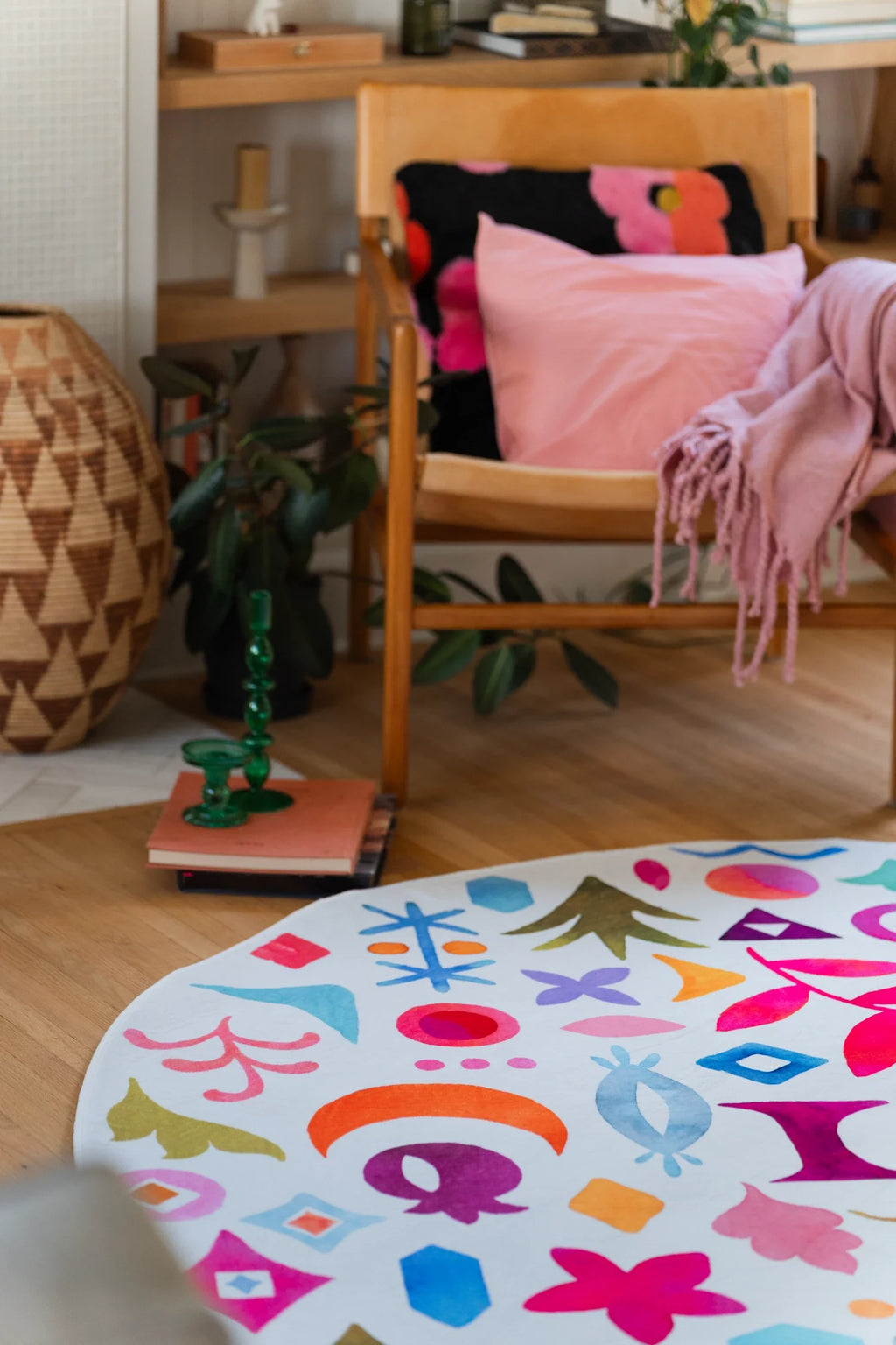 Partial view of the colorful round rug beside a wood chair, with birds, flowers, and abstract icons across the surface