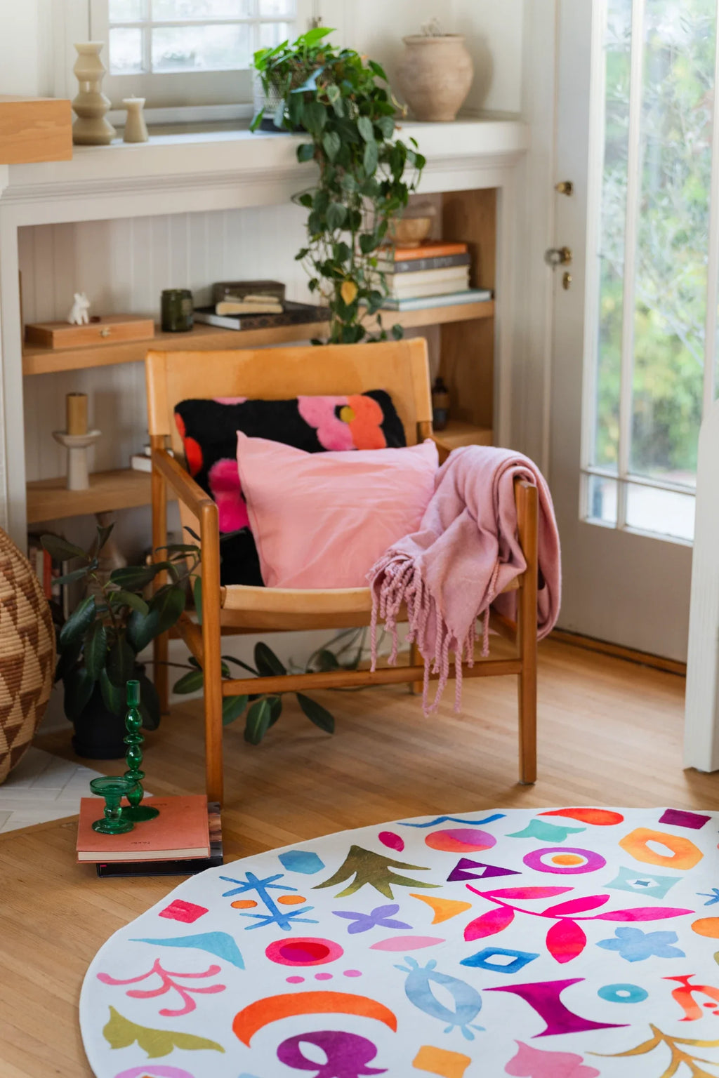 Round graphic area rug under a wood chair with pink cushions, showing colorful botanical and geometric symbols on a white ground