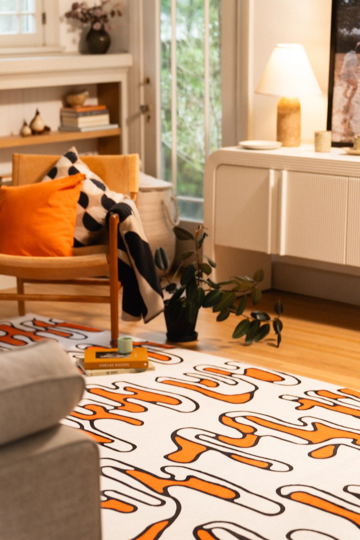 Beige graphic rug beneath a wooden armchair in a sunlit living room near a gray sofa.