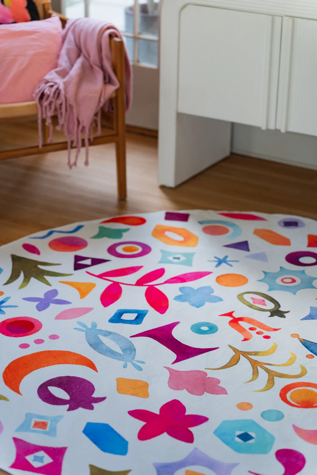 Colorful graphic pattern round rug near white cabinetry, with scattered stars, leaves, birds, and curved shapes