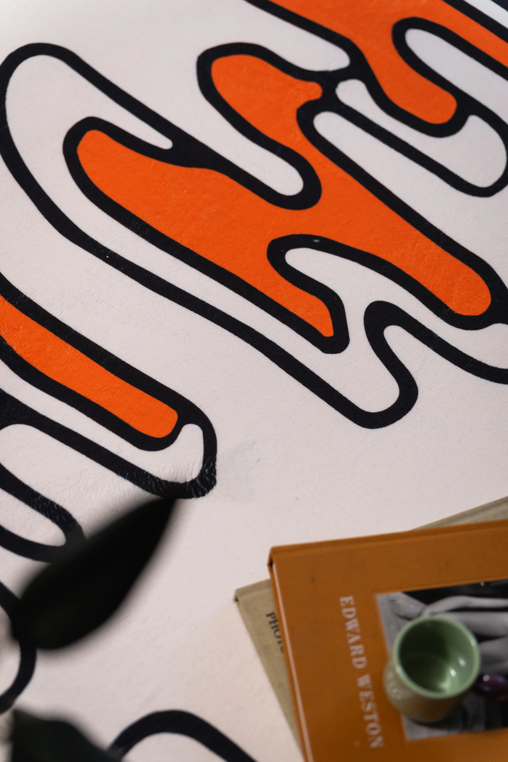 Orange and black looping pattern on a beige rug beside a book and green cup.