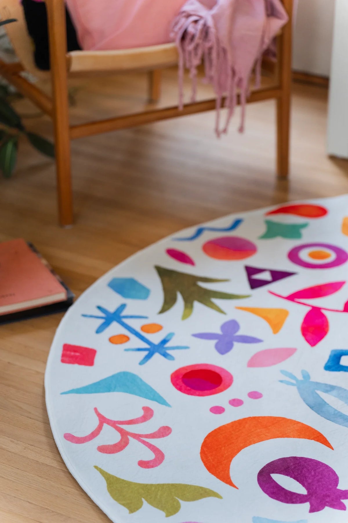 Close crop of the round rug under a chair edge, showing bright red, blue, orange, and pink symbols on a white field