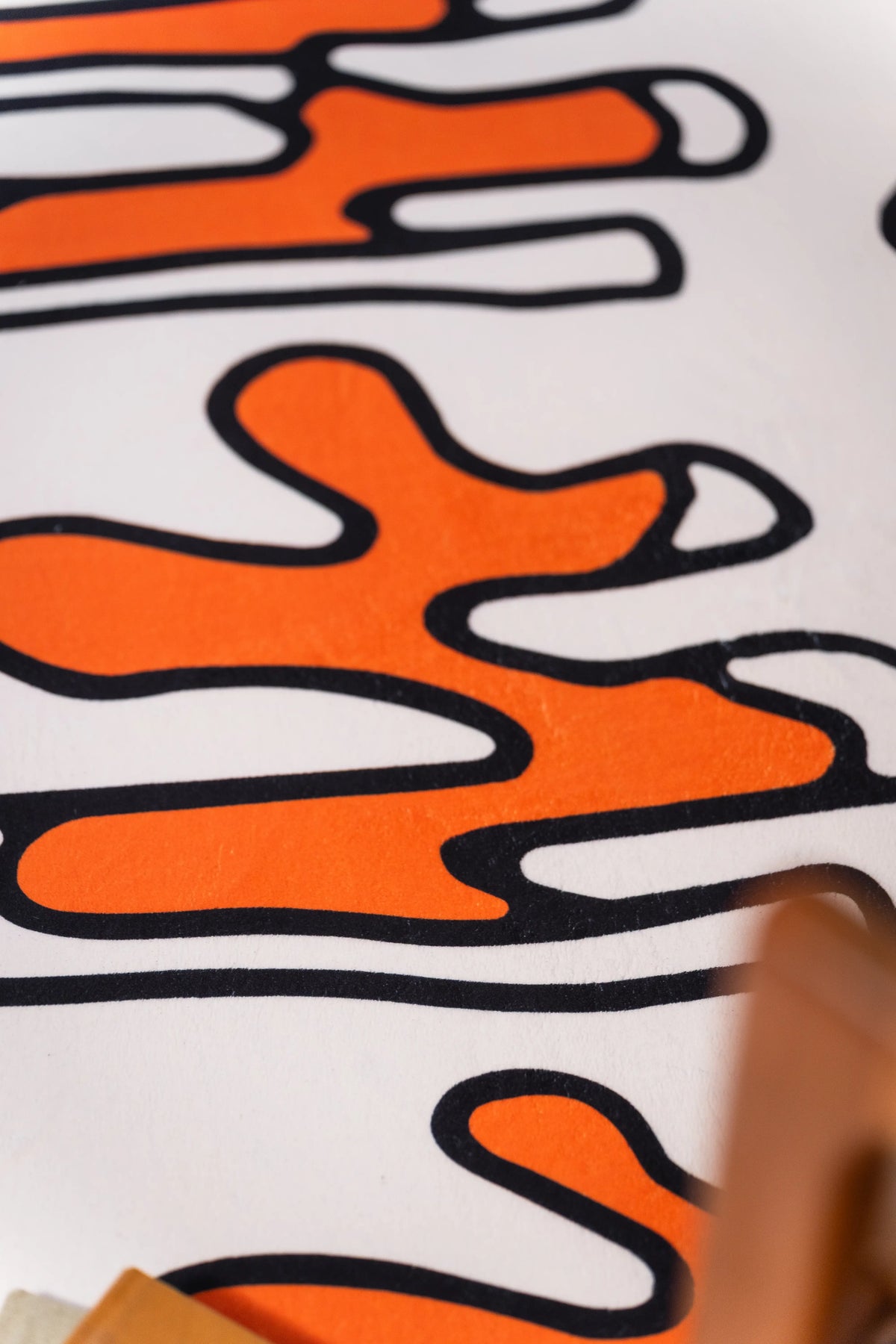 Close-up of orange squiggles outlined in black on a beige rug beside a wooden chair.
