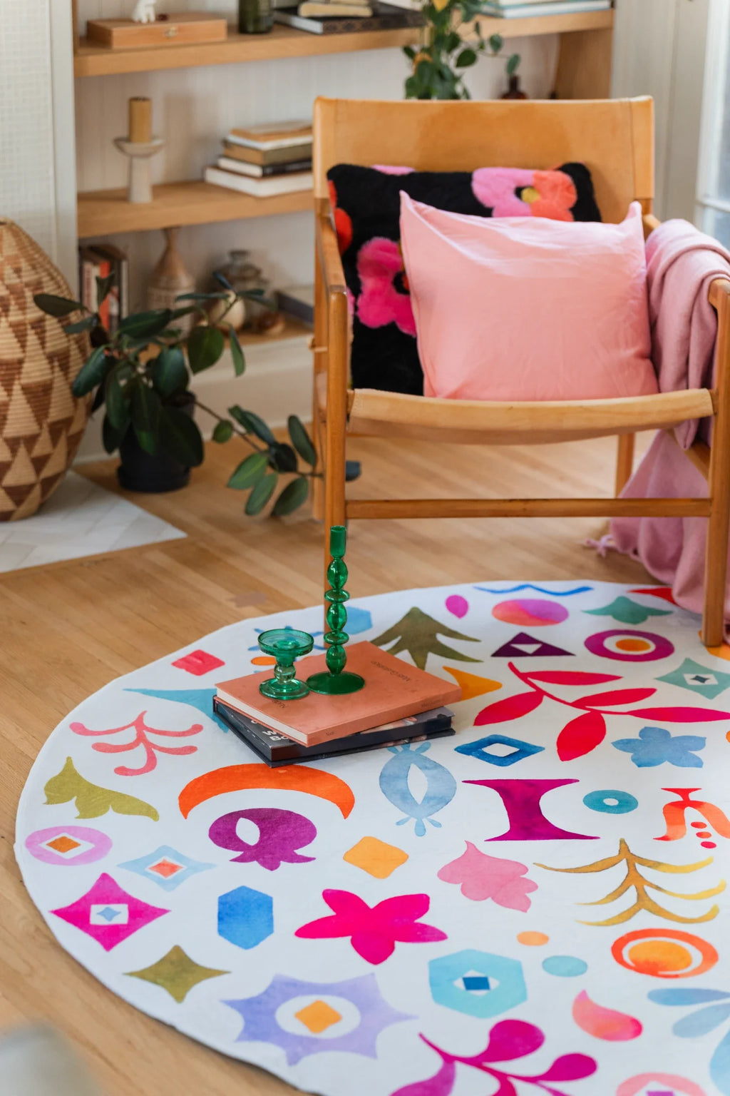 Colorful graphic pattern round rug beside a wood chair and open shelving on a light wood floor in a cozy reading corner