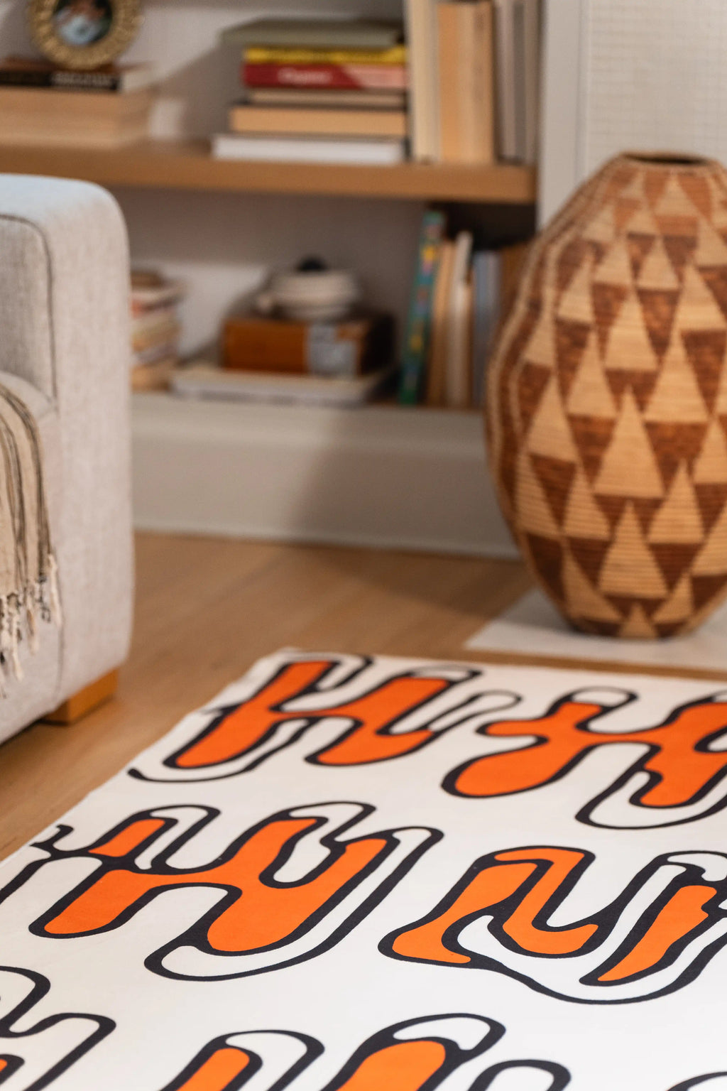 Close-up of a beige rug with orange loops beside a gray sofa and geometric wooden vase.