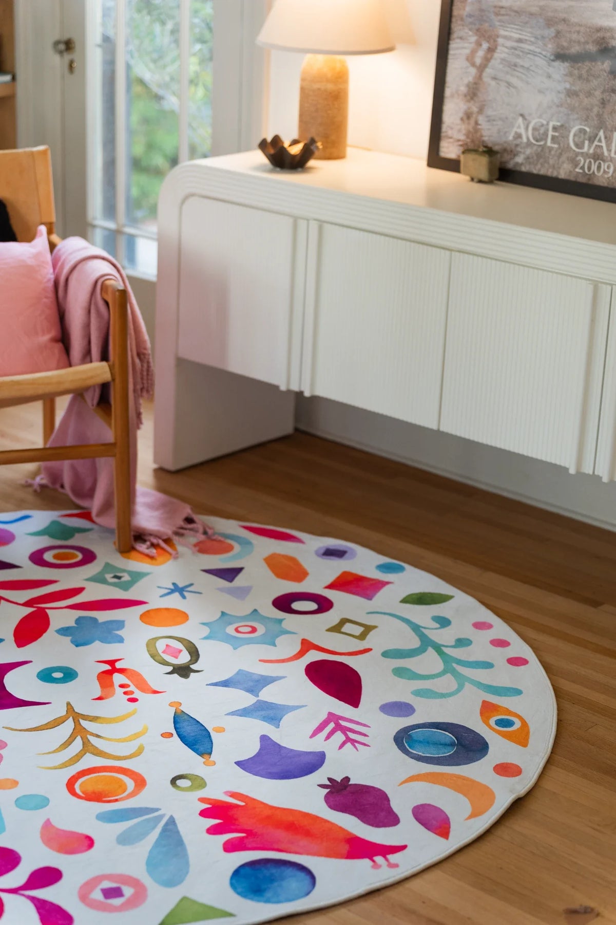 Graphic pattern round rug in a bright corner with a white media console, lamp, and light wood floor