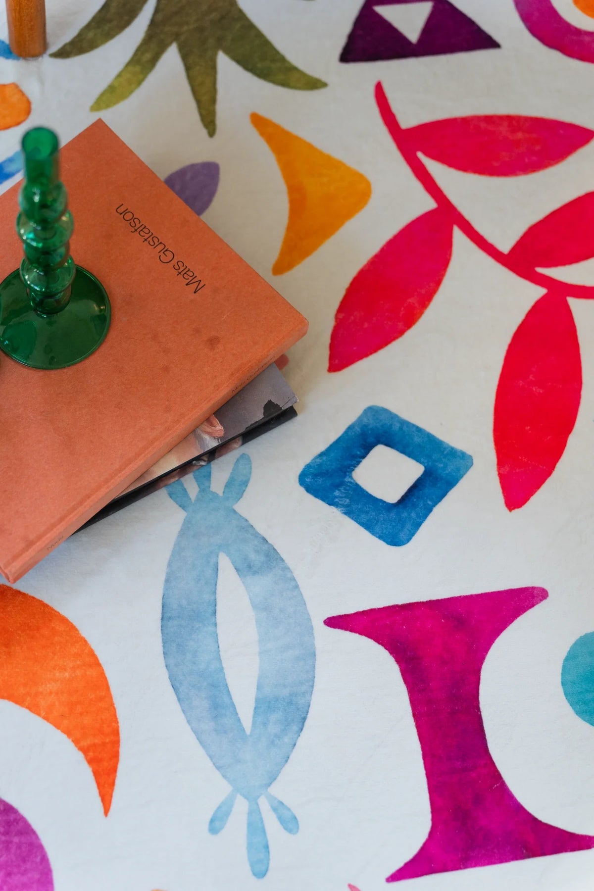 Close up of the colorful round rug with a green lamp base, showing red leaves, blue bird shapes, and geometric icons