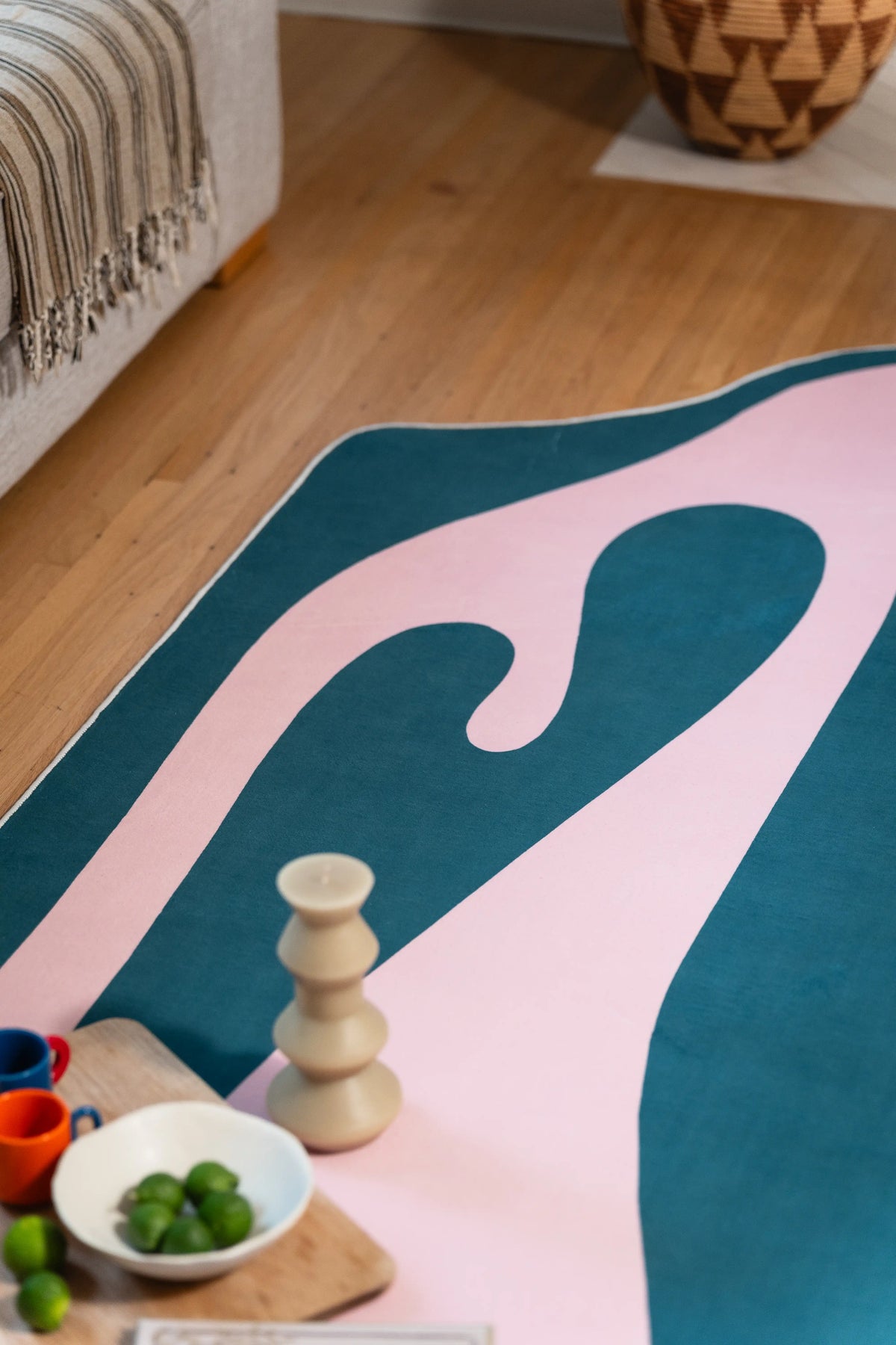 At the sofa edge, the pink ribbon folds into a rounded loop on blue beside a candle and bowl of green fruit.