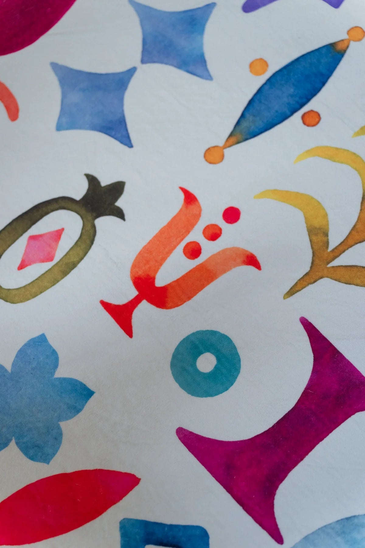 Detail of the round graphic rug with blue botanical forms, red leaf shapes, and small abstract symbols on white