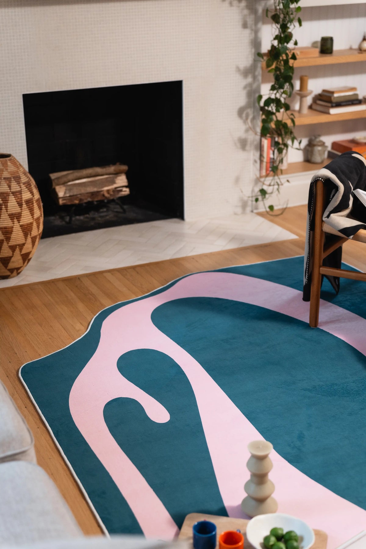 Seen from beside the fireplace, a pale pink ribbon loops across the blue rug toward a wooden armchair.