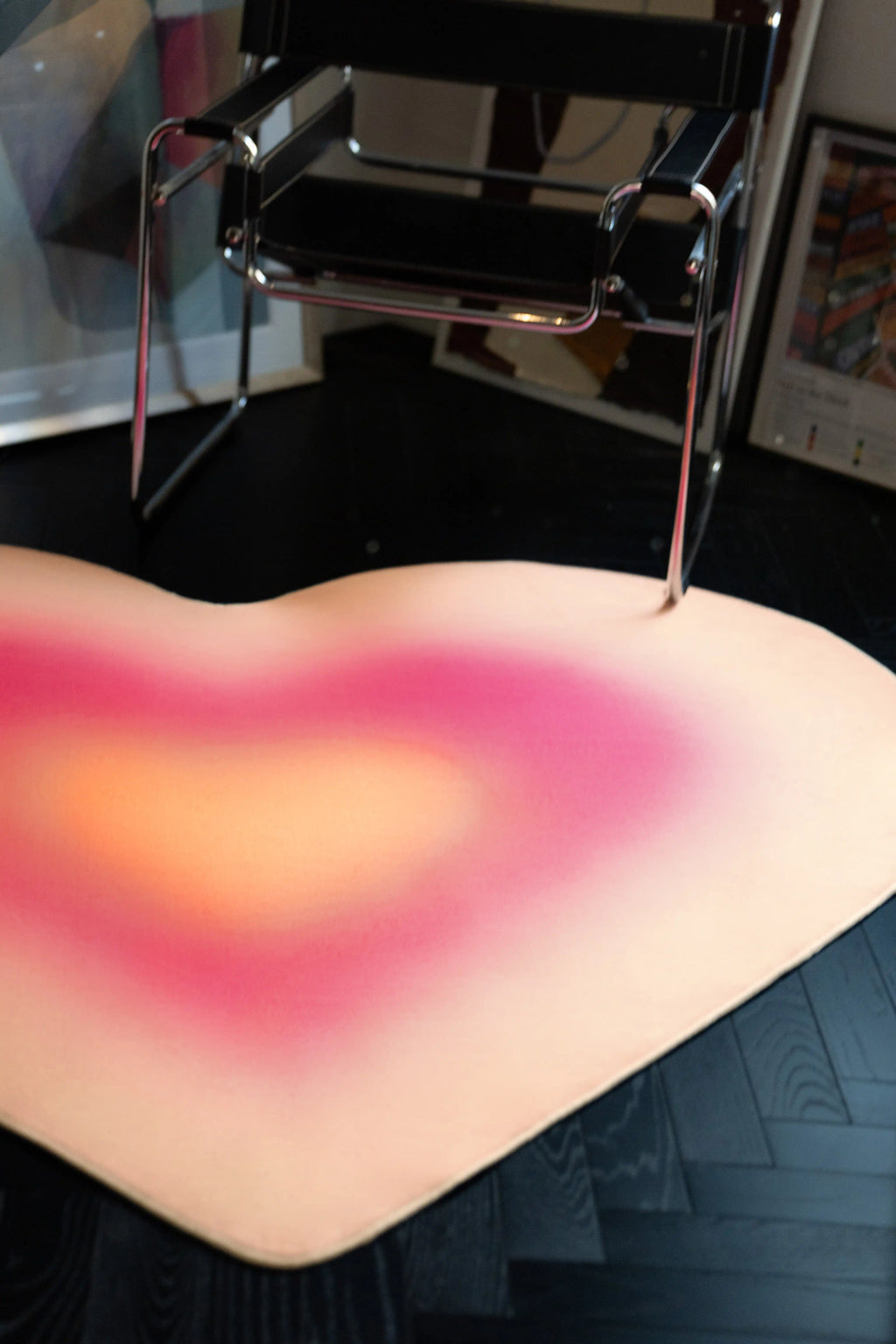 Pink Modern Gradient Heart Rug tucked under a chrome chair on a dark herringbone wood floor