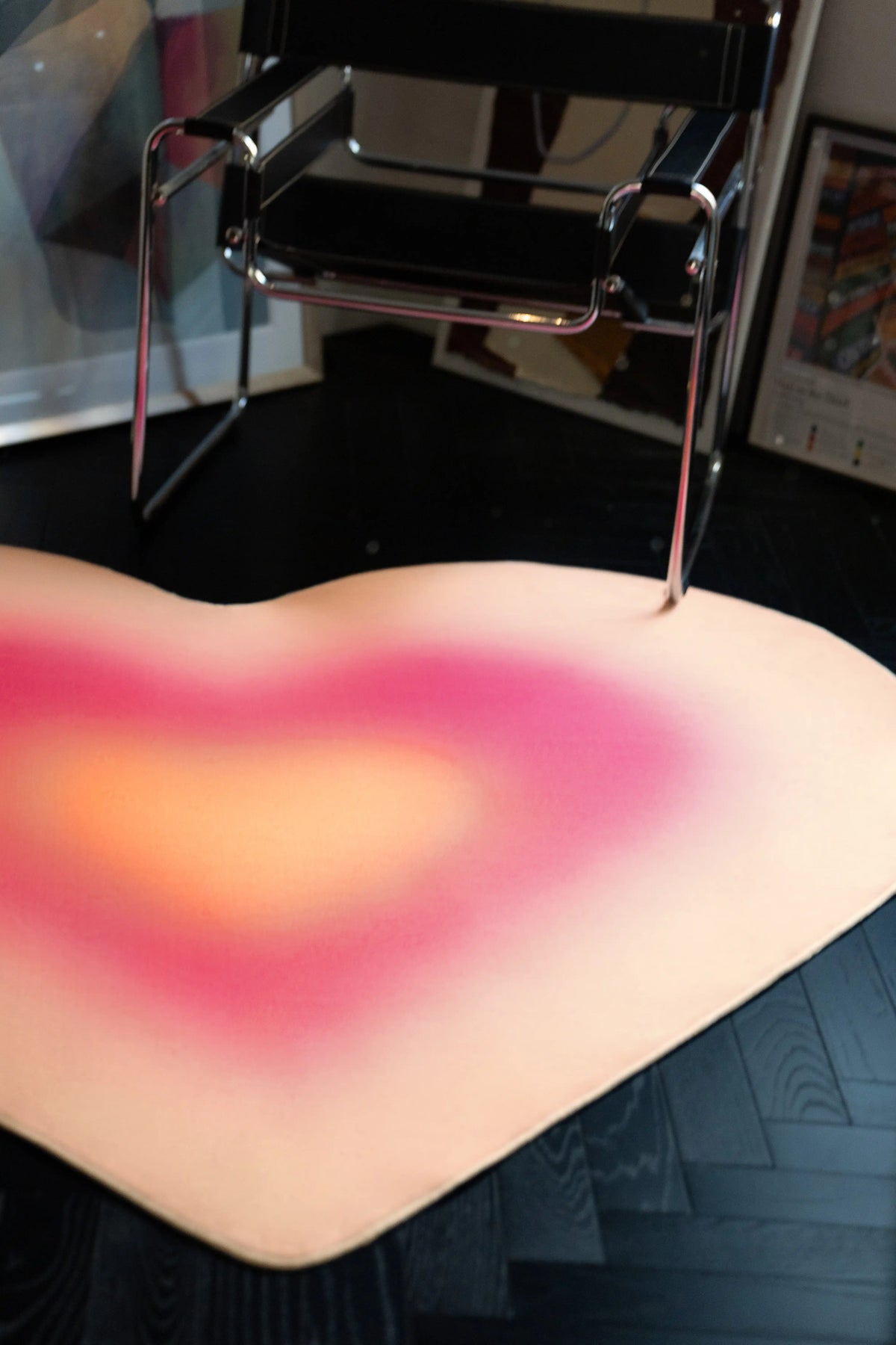Pink Modern Gradient Heart Rug tucked under a chrome chair on a dark herringbone wood floor
