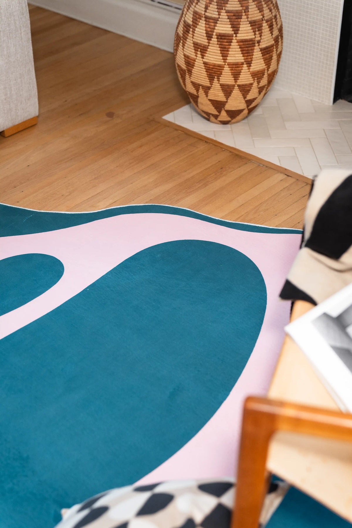 Close crop of the blue field and pink curve beside a geometric wooden vase and wooden chair leg.