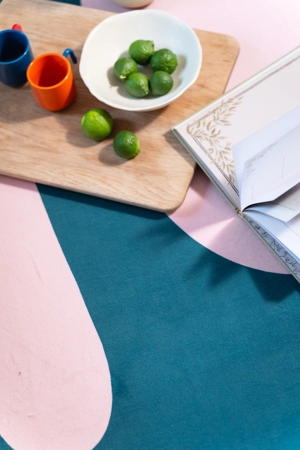 Top-down view of a tray, green fruit, orange cup, and newspaper resting where pink meets blue on the rug.