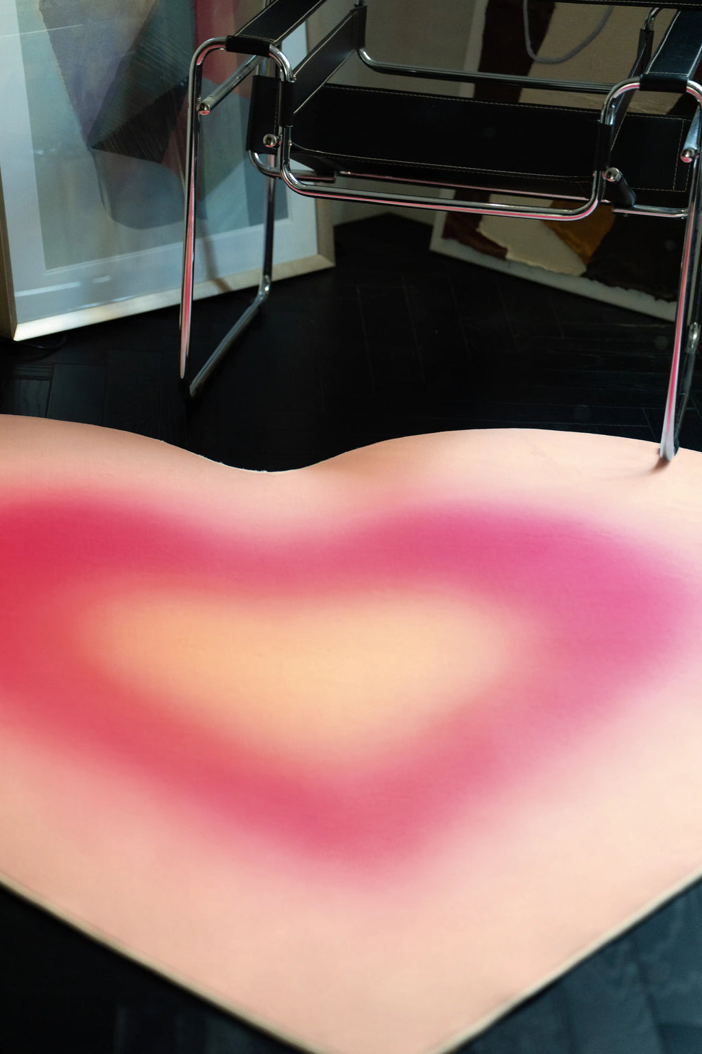 Close up of the gradient heart rug beneath a chrome chair showing pink, peach, and yellow tonal layers