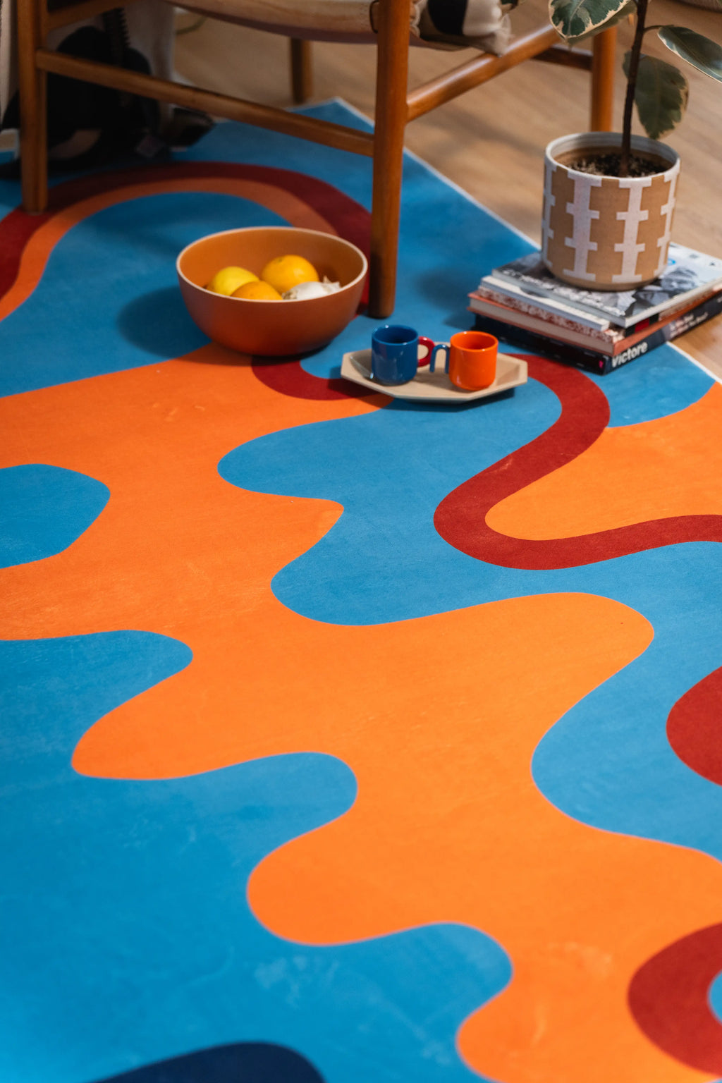 A rust-red ribbon winds between orange and blue wave blocks, ending near a tea tray and books.