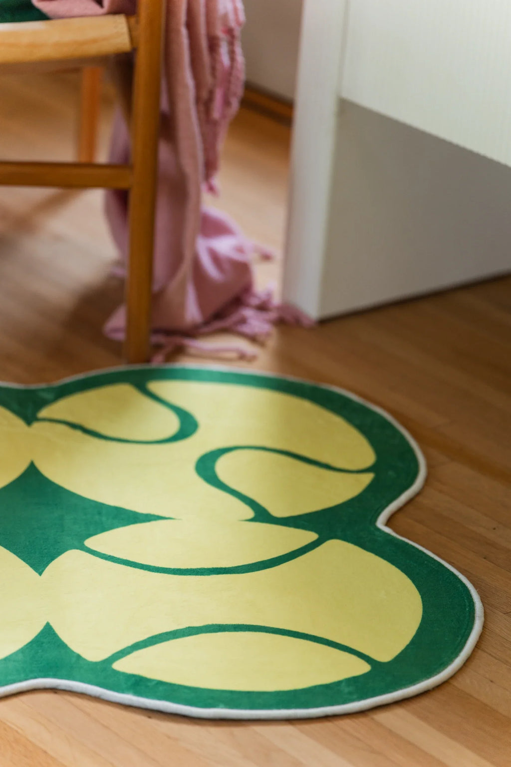 Corner crop of the yellow rug under a wood chair with a pink throw, showing playful tennis inspired curves