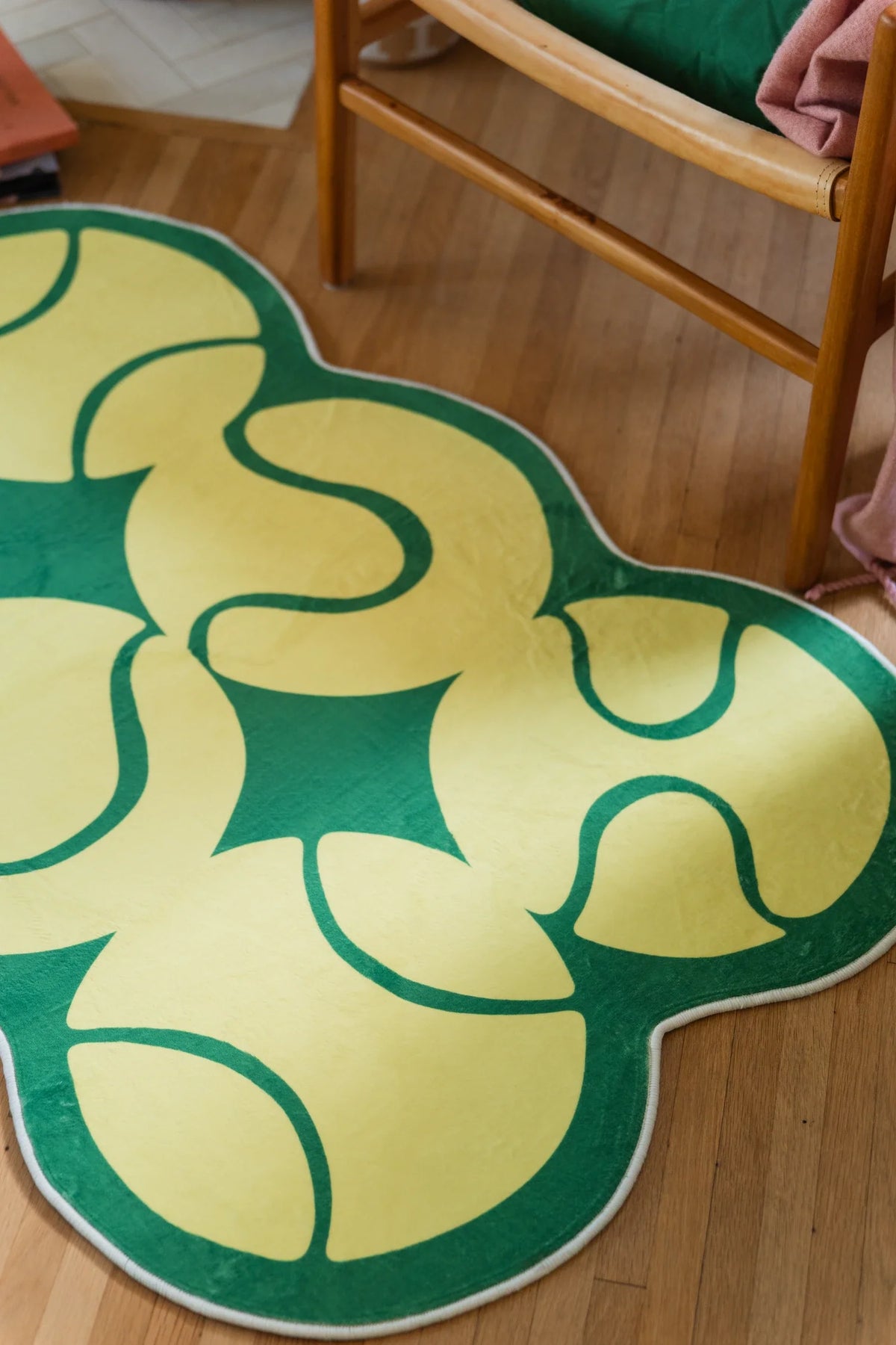 Close up of the yellow rug beneath a wood chair, showing looping green court lines and rounded edges