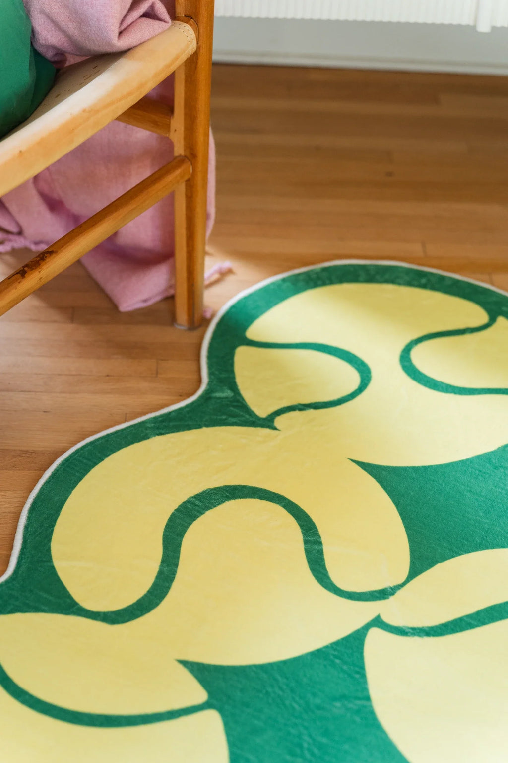 Close view of the irregular yellow rug beneath a wood chair on a light wood floor