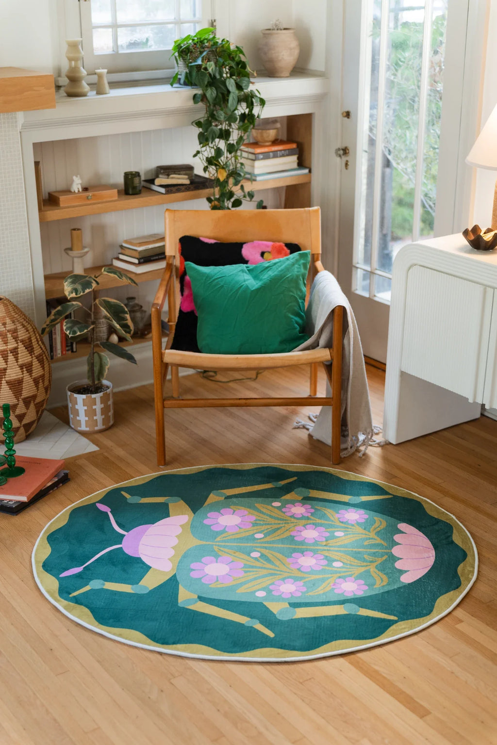 Green graphic beetle floral round rug in a cozy reading corner with a wood chair, open shelving, and a light wood floor