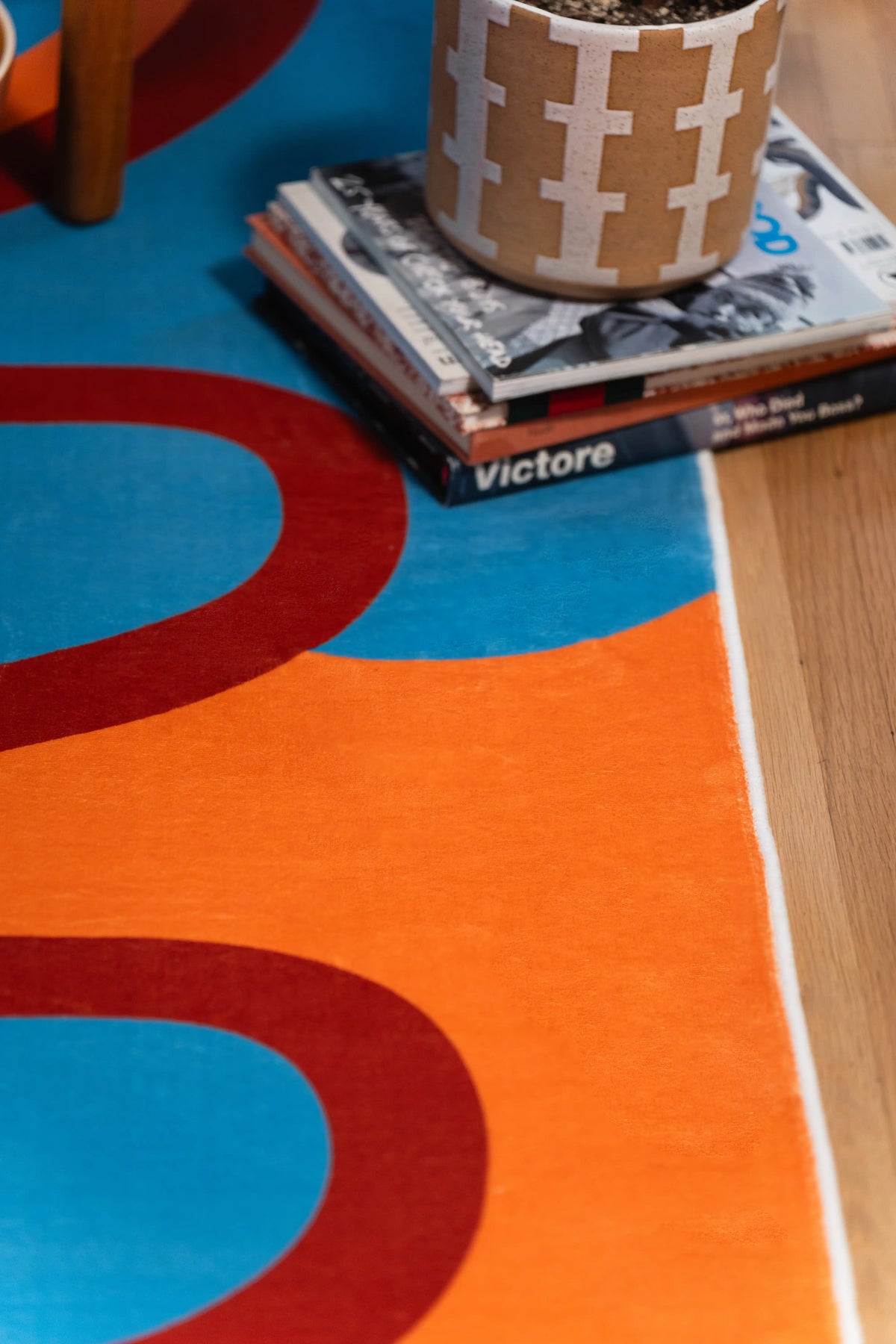 Close-up of the rug’s bound edge on a wood floor, where a red loop separates blue and orange sections.