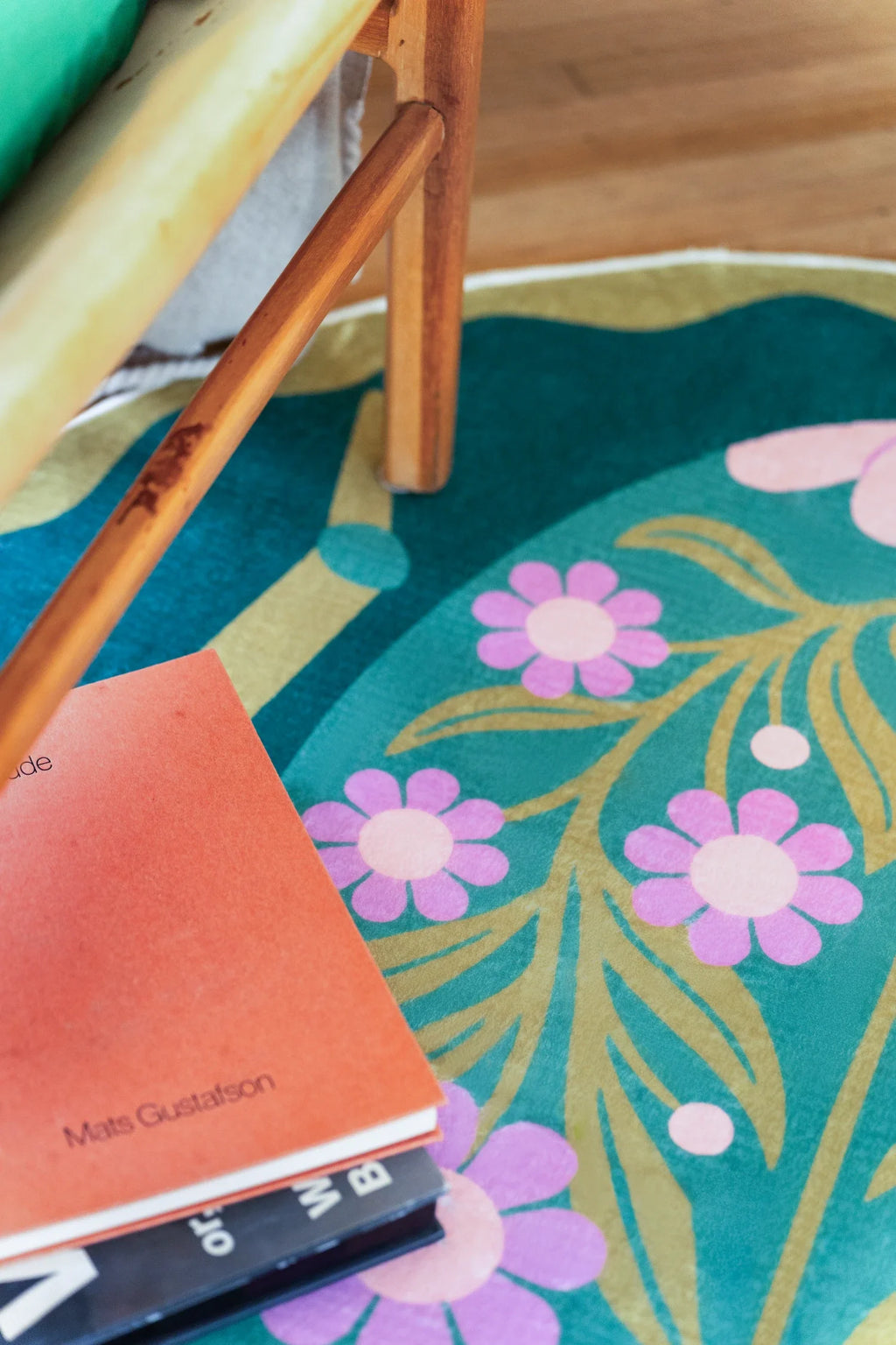 Close up beneath a wood chair, showing pink flowers and pale green stems across the deep green round rug