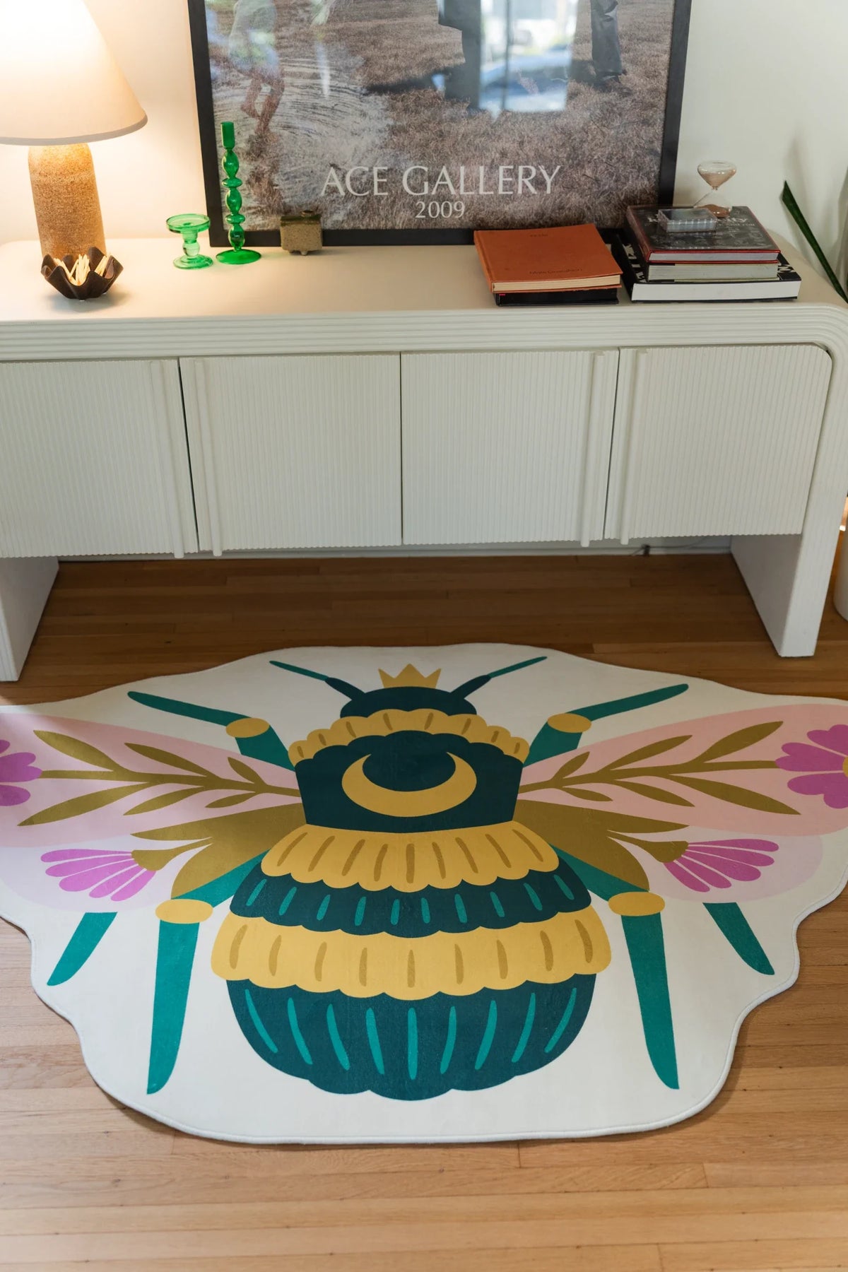 Colorful bee shaped rug centered in front of a white cabinet, showing teal wings, a yellow body, and pink floral details