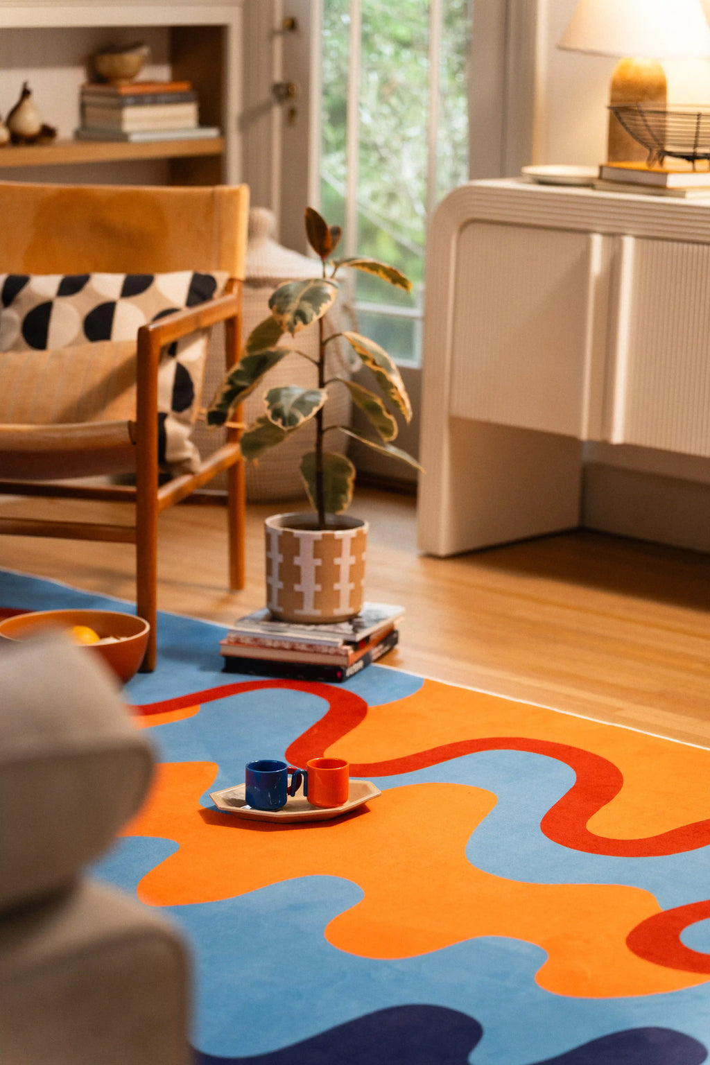 Seen from behind the gray sofa, orange and blue waves continue toward a wooden chair and white cabinet.