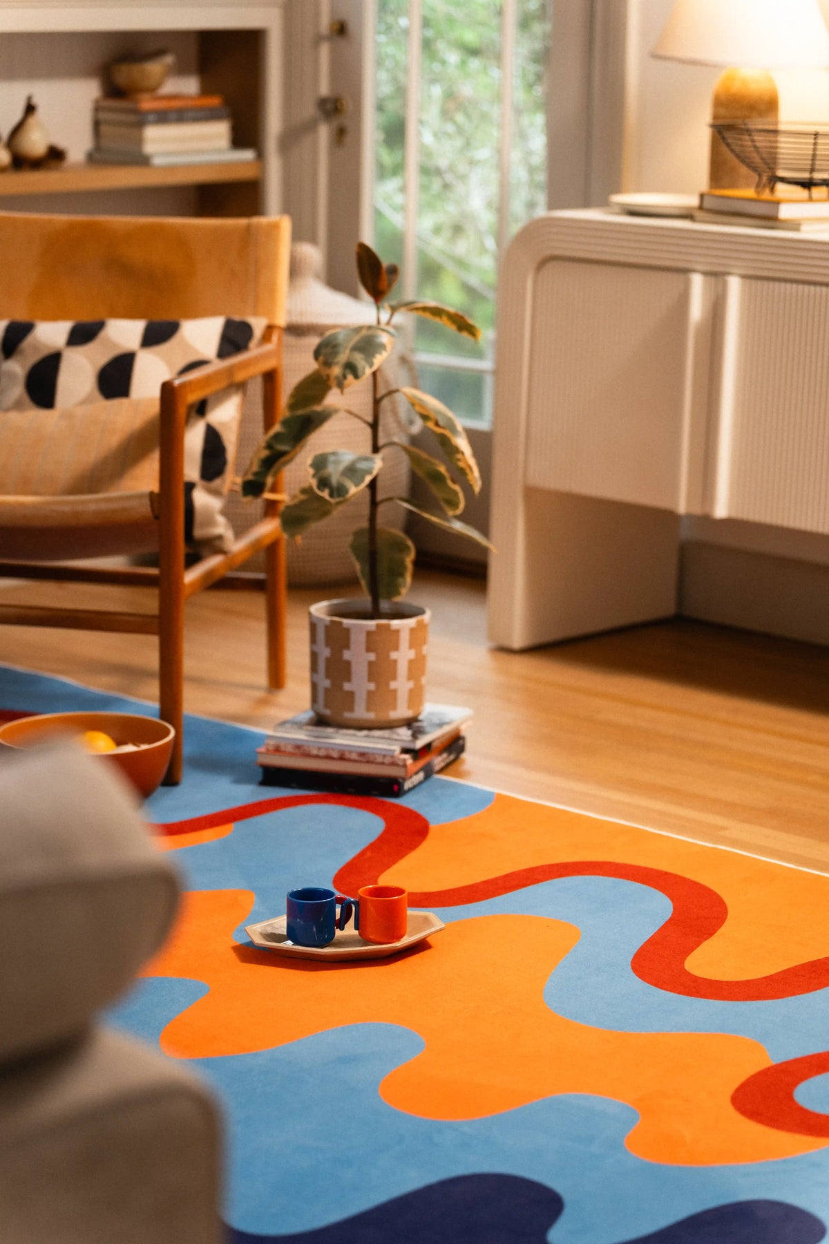 Seen from behind the gray sofa, orange and blue waves continue toward a wooden chair and white cabinet.