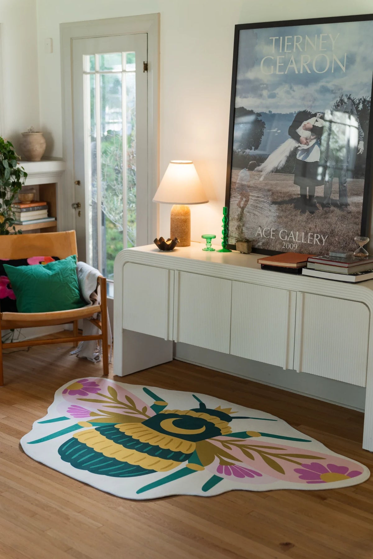 Colorful graphic queen bee shaped rug on a light wood floor beside a white media console and wood chair