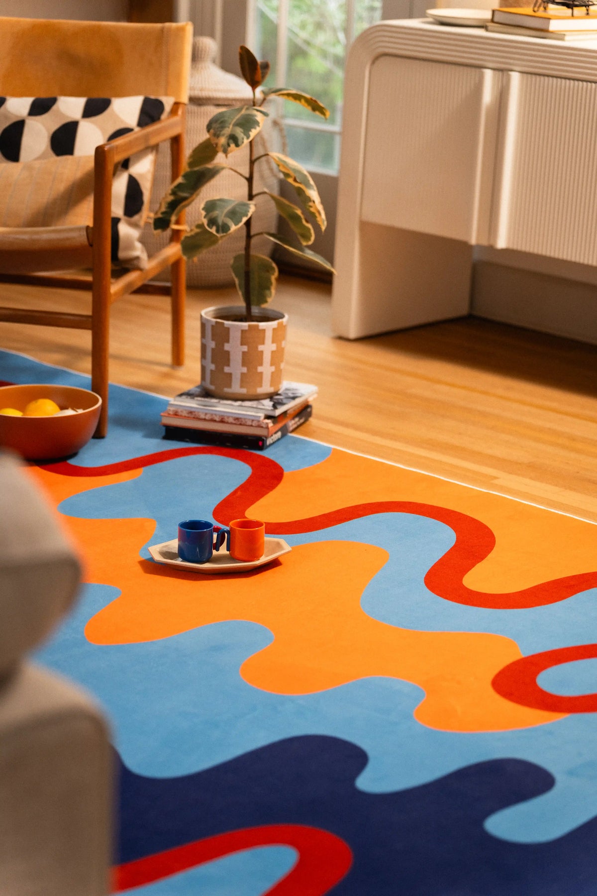 A low corner view follows the orange wave past a tea tray toward the chair and white cabinet.
