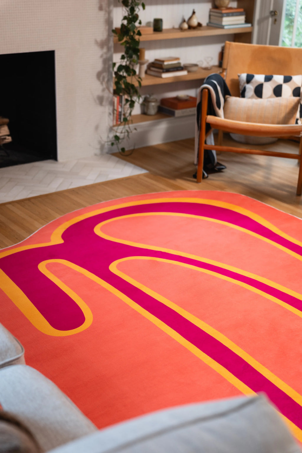 Coral orange rug with a yellow-edged magenta stripe beneath a wooden armchair beside a fireplace.