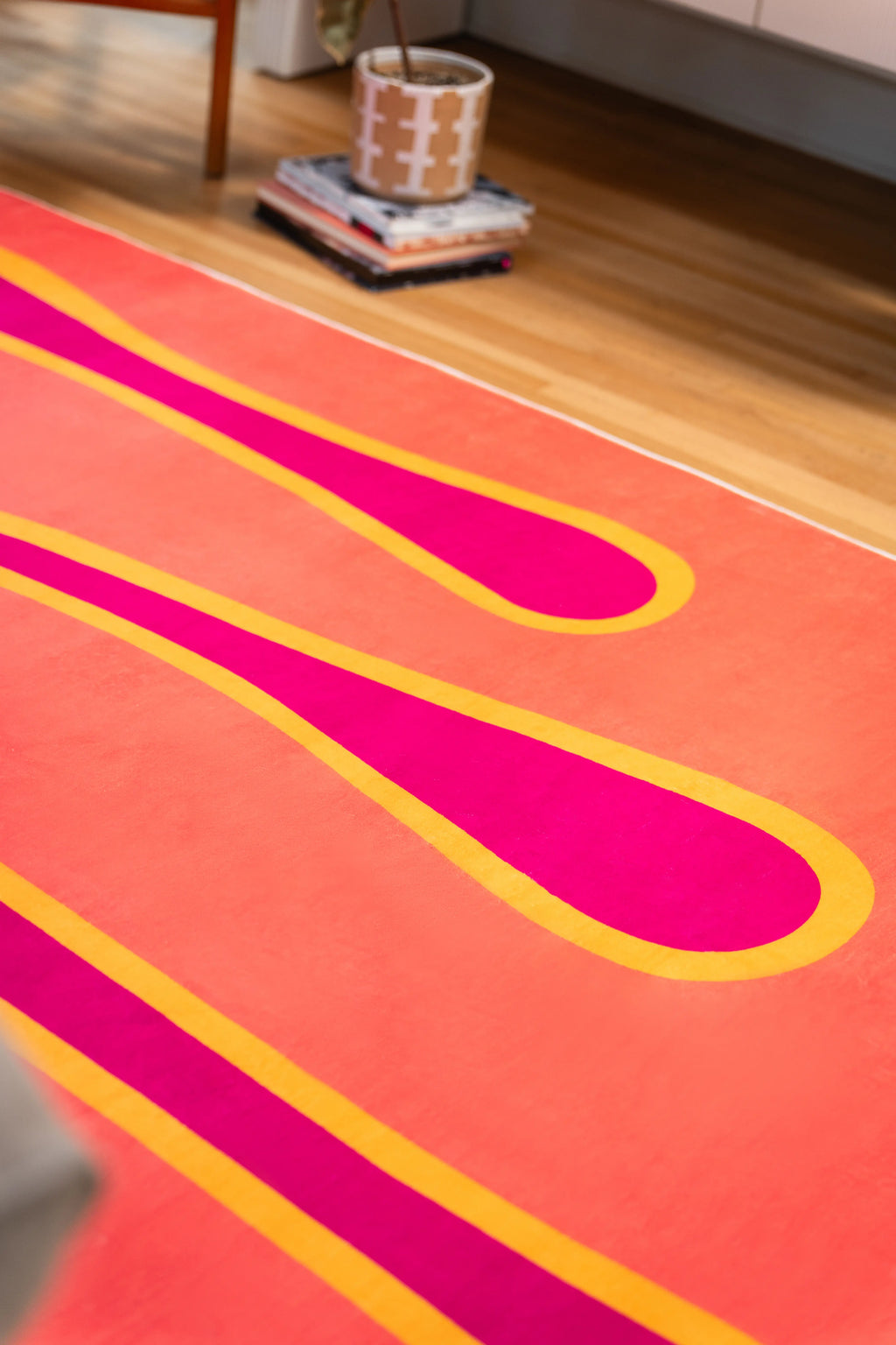Close-up of a magenta melting stripe outlined in yellow across a coral orange rug on light wood flooring.