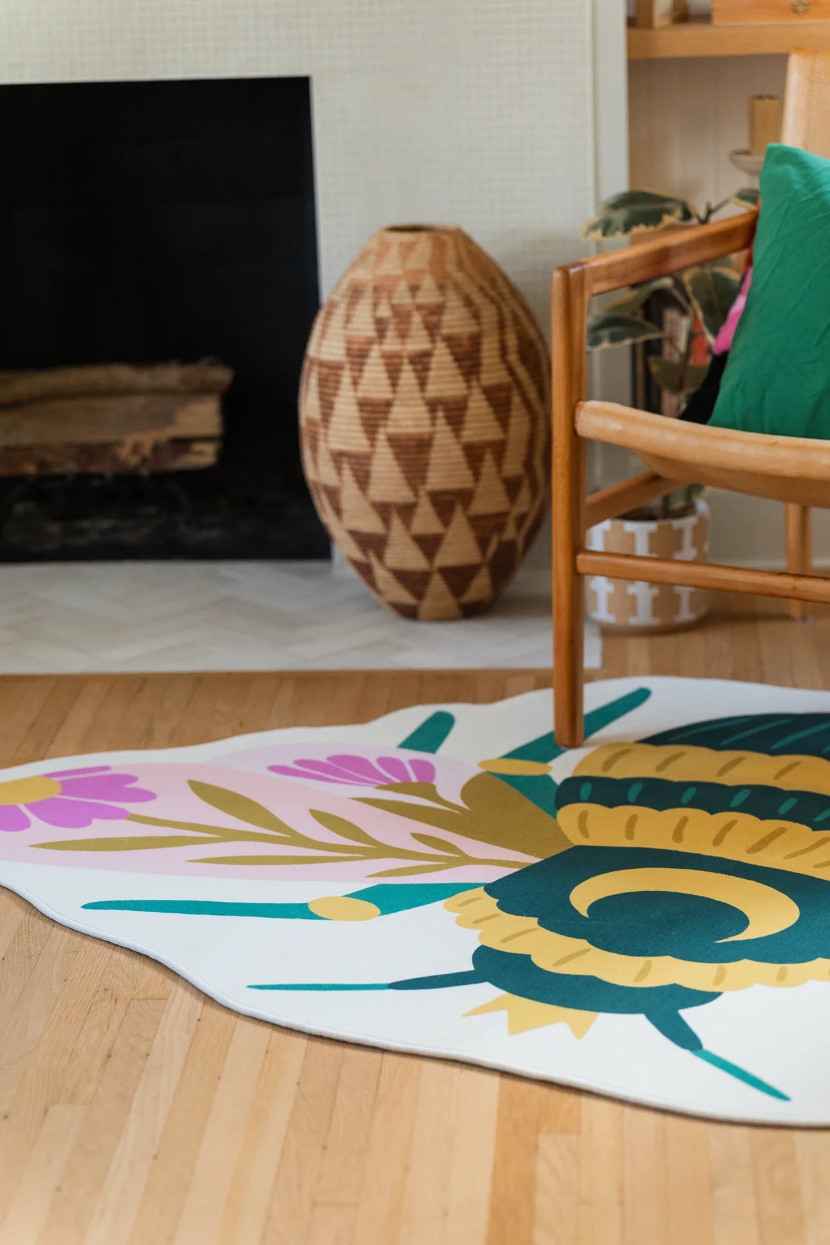 Colorful irregular shaped rug near the fireplace and wood chair, with a queen bee silhouette on a light wood floor
