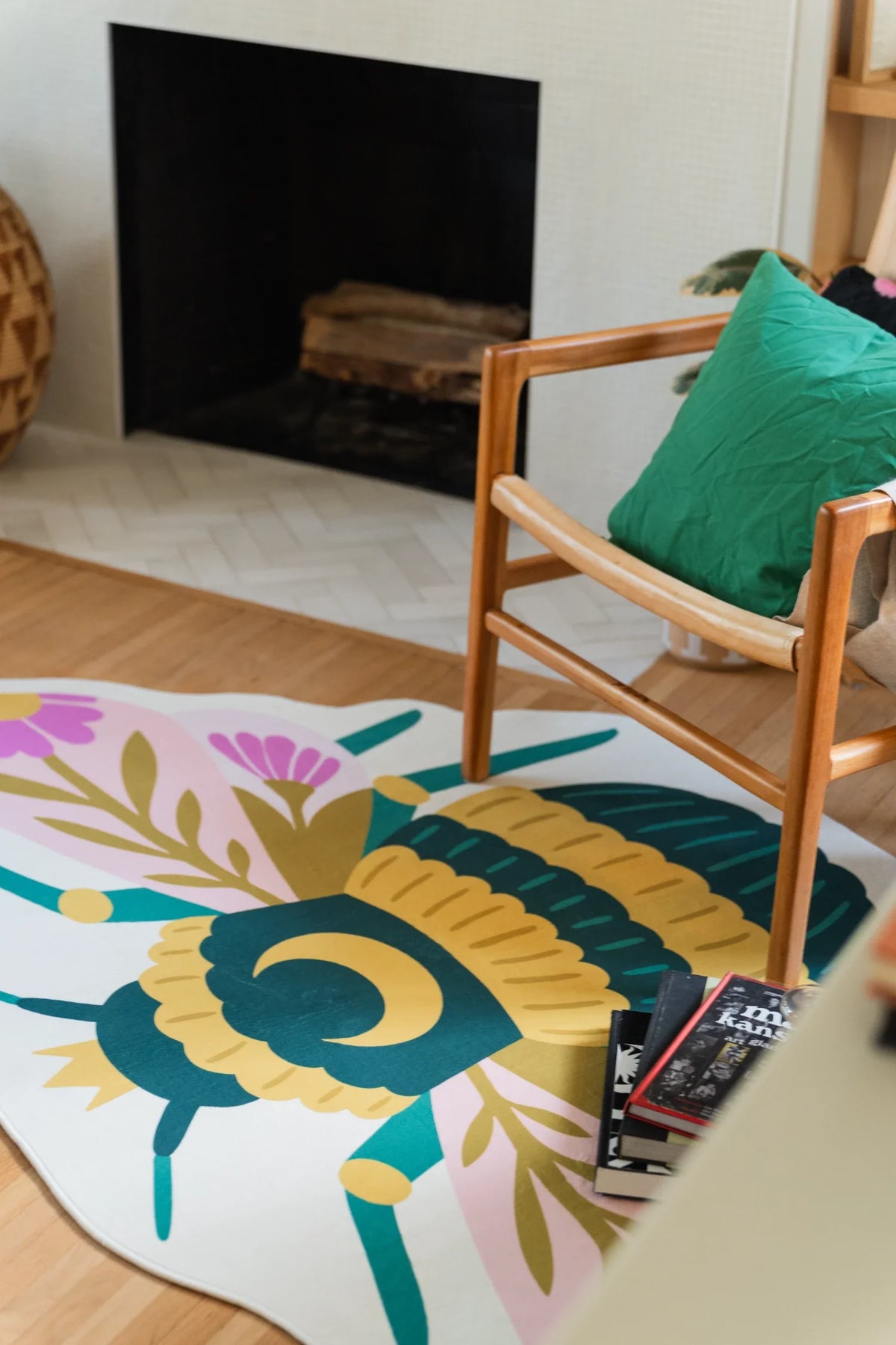 Close crop of the graphic bee rug beside a wood chair, highlighting the yellow body, teal bands, and pink floral wings