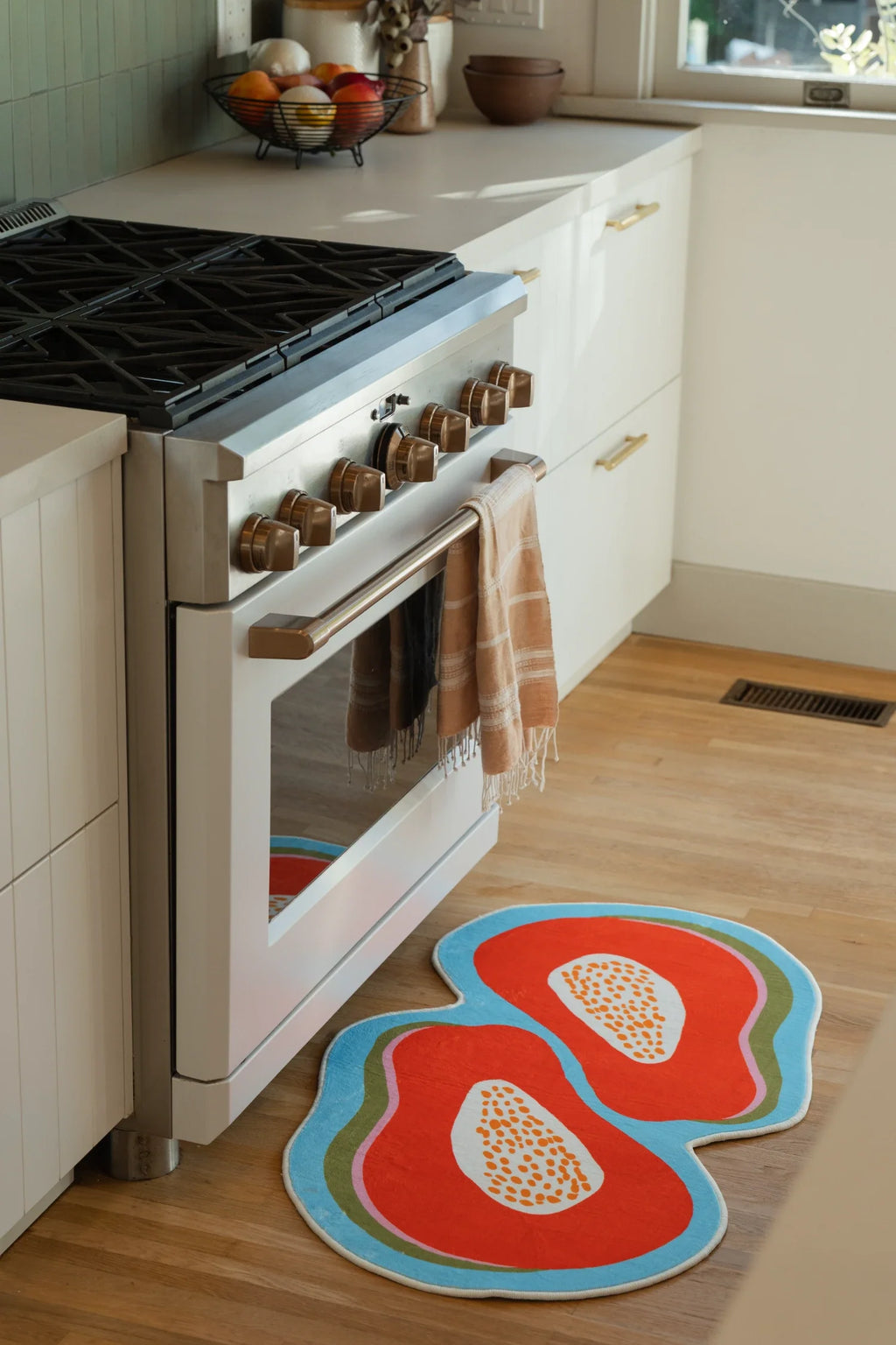 Papaya rug beside a white oven in a bright kitchen with light wood floor and white cabinetry