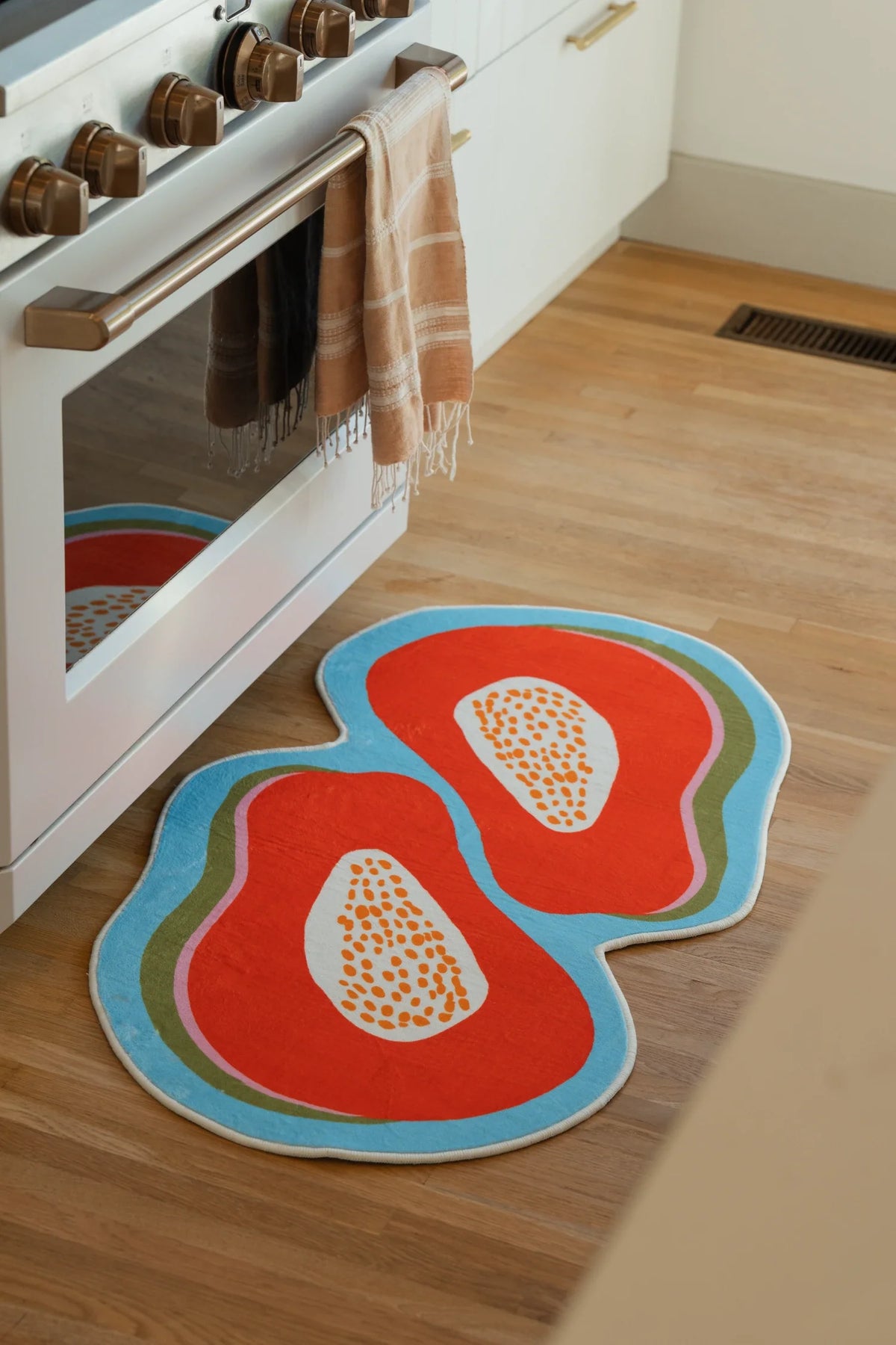 Papaya Orange Irregular Fruit Rug by Zoe Wodarz beside a white kitchen oven on a light wood floor