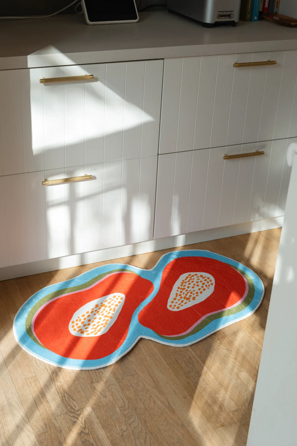 Papaya fruit rug in sunlight beside white lower cabinets, showing orange forms and pale seed centers