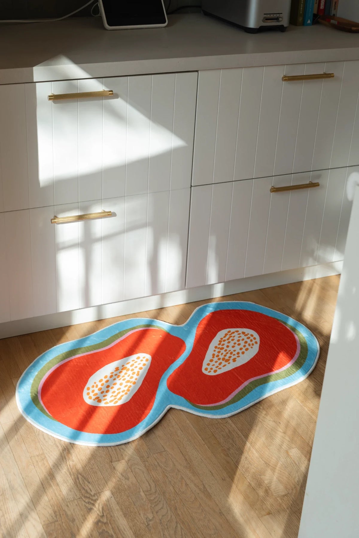 Papaya fruit rug in sunlight beside white lower cabinets, showing orange forms and pale seed centers