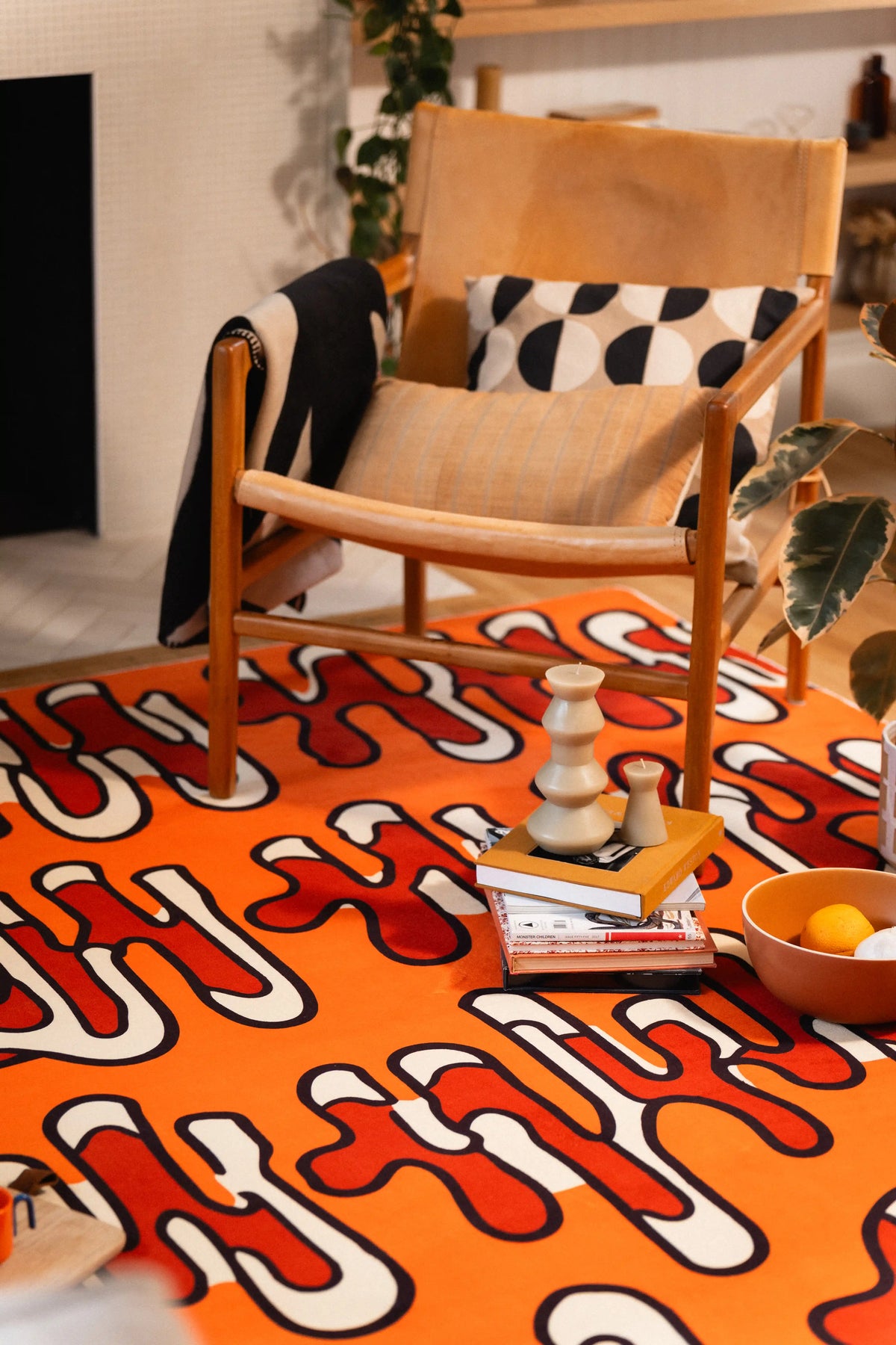 Orange graphic rug beneath a wooden armchair with books, a candle, and a bowl arranged in front.