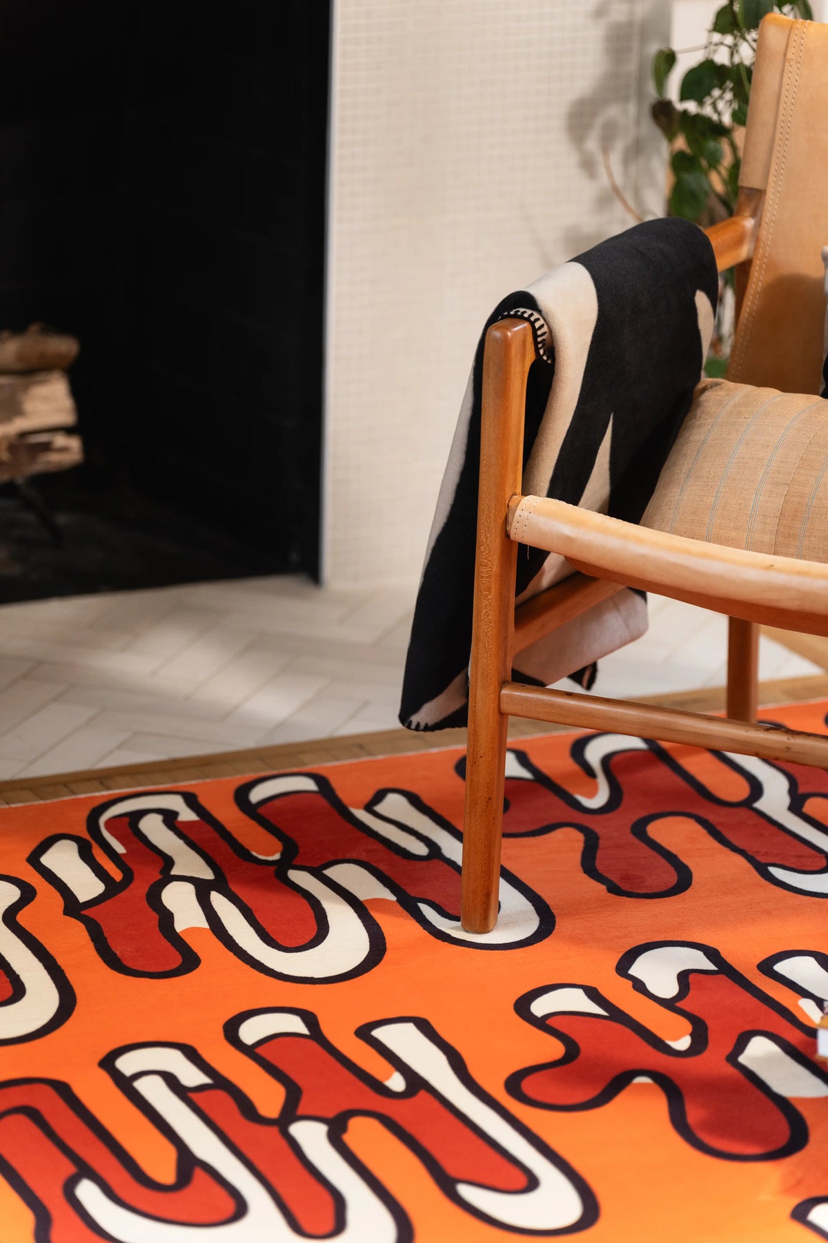 Black-outlined red and cream loops on an orange rug beneath a wooden chair by the fireplace.