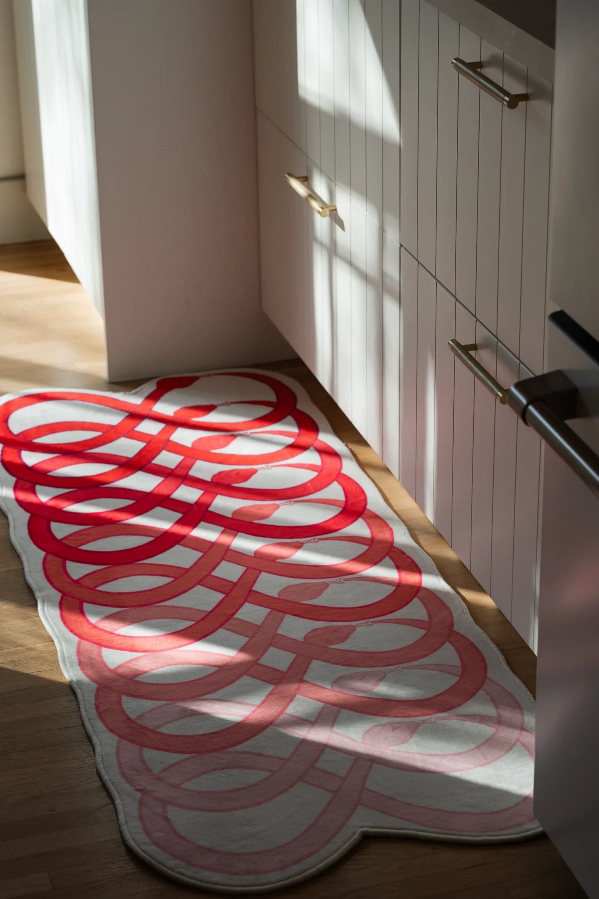 Long view of the abstract runner rug beside white lower cabinets, with repeated red loops leading down the hallway
