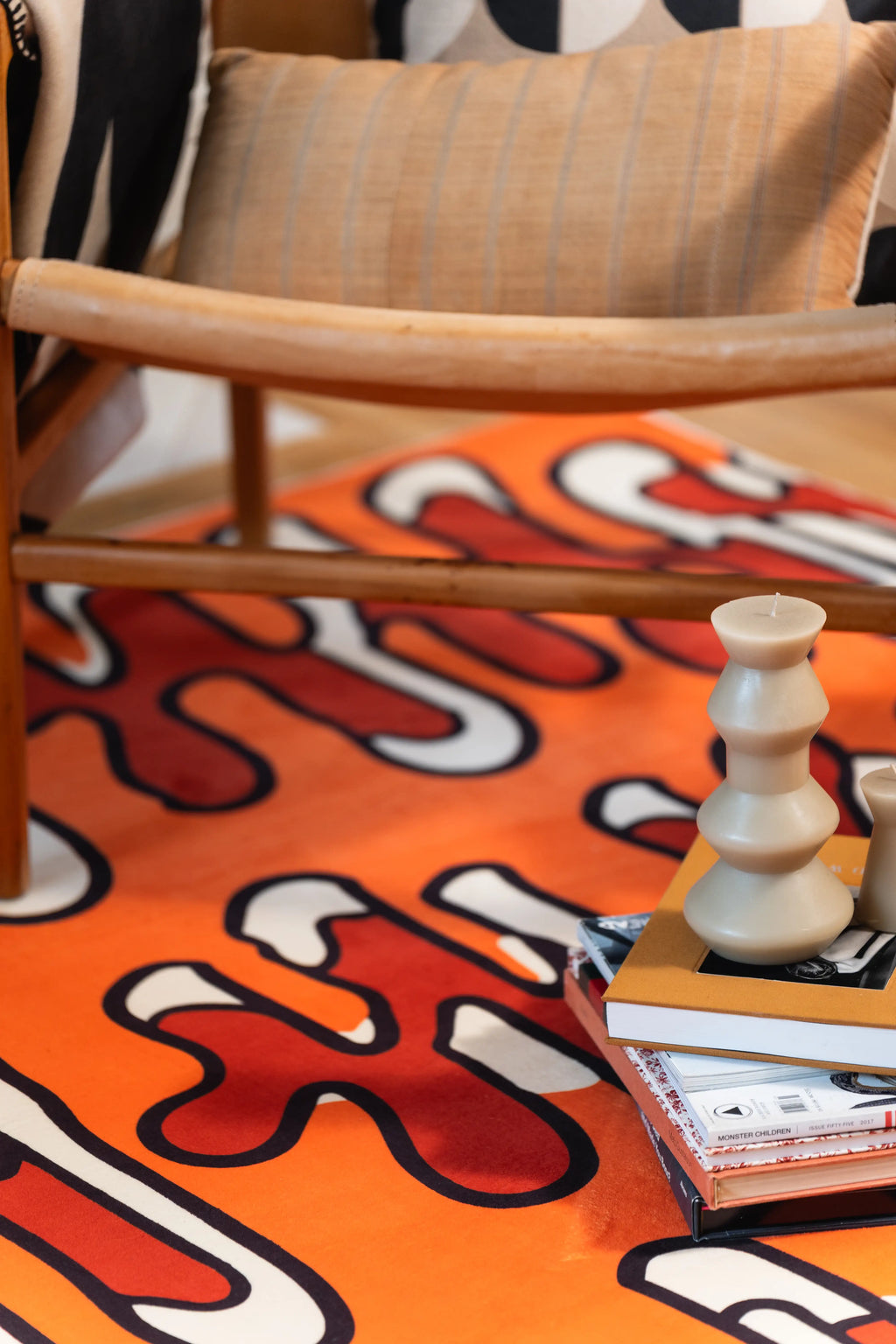 Close-up of an orange rug beneath a chair with stacked books and a sculptural candle.