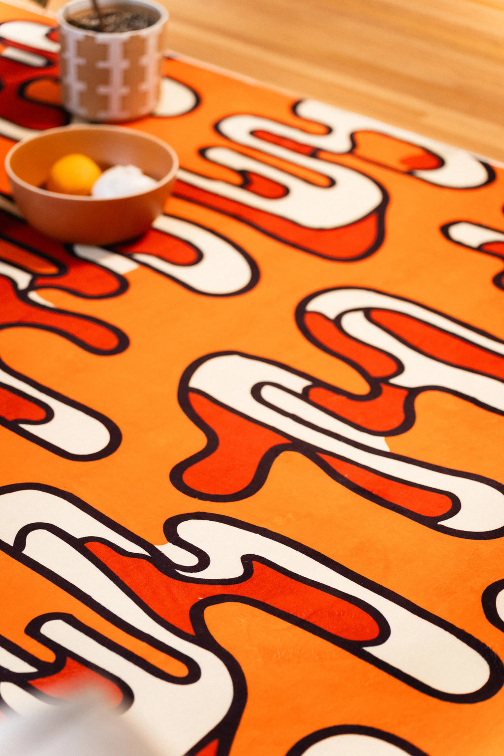 Cream and red looping shapes on an orange rug beside a bowl and patterned mug.