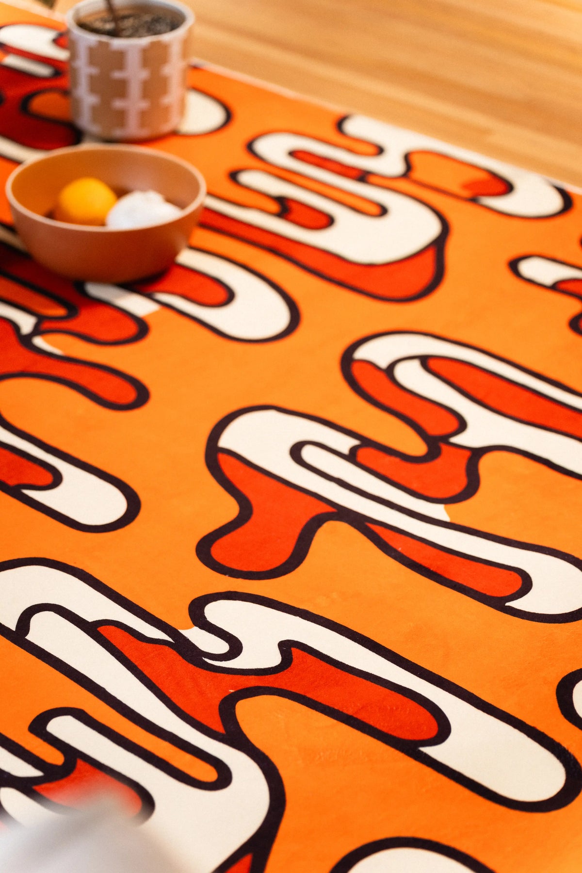 Cream and red looping shapes on an orange rug beside a bowl and patterned mug.