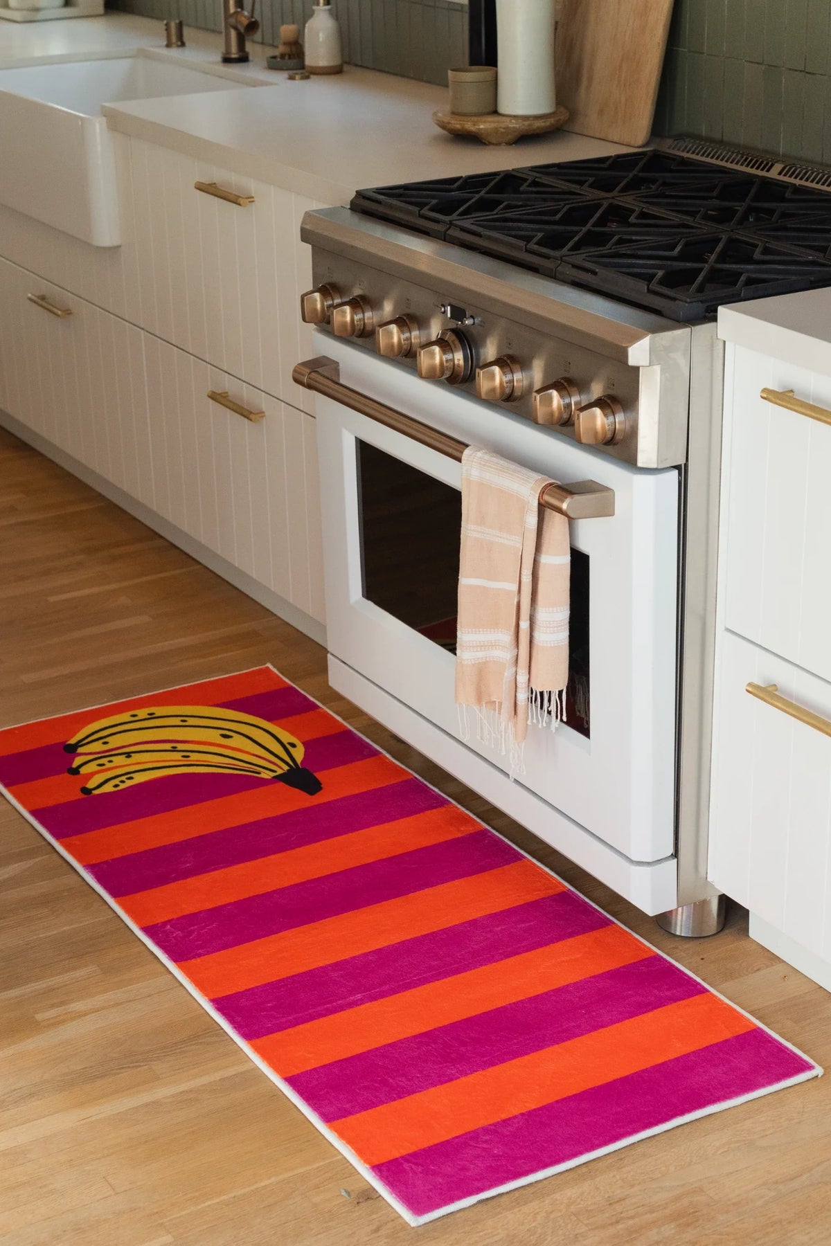 Striped banana kitchen runner placed in front of a white oven, showing magenta, pink, and orange bands