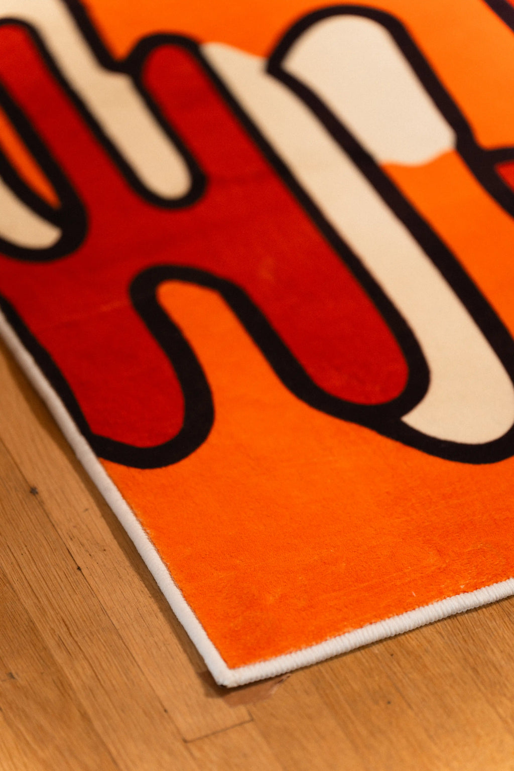 Bound corner of an orange rug with a black, red, and cream abstract pattern on wood flooring.