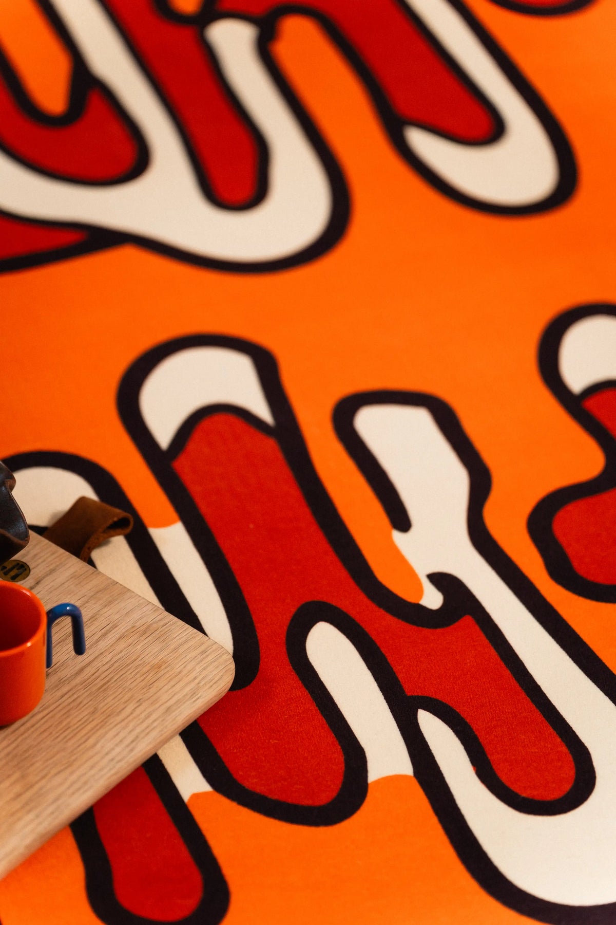 Close-up of black-outlined red and cream loops on a bright orange rug beside wooden furniture.