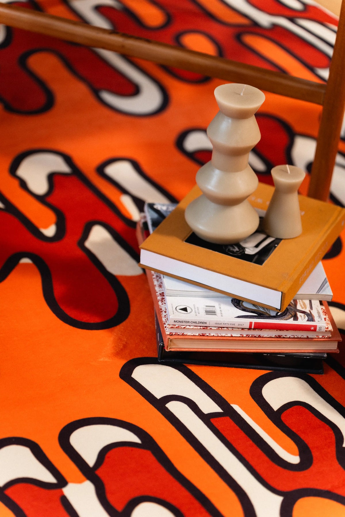 Top view of an orange abstract rug beside stacked books and a white sculptural candle.